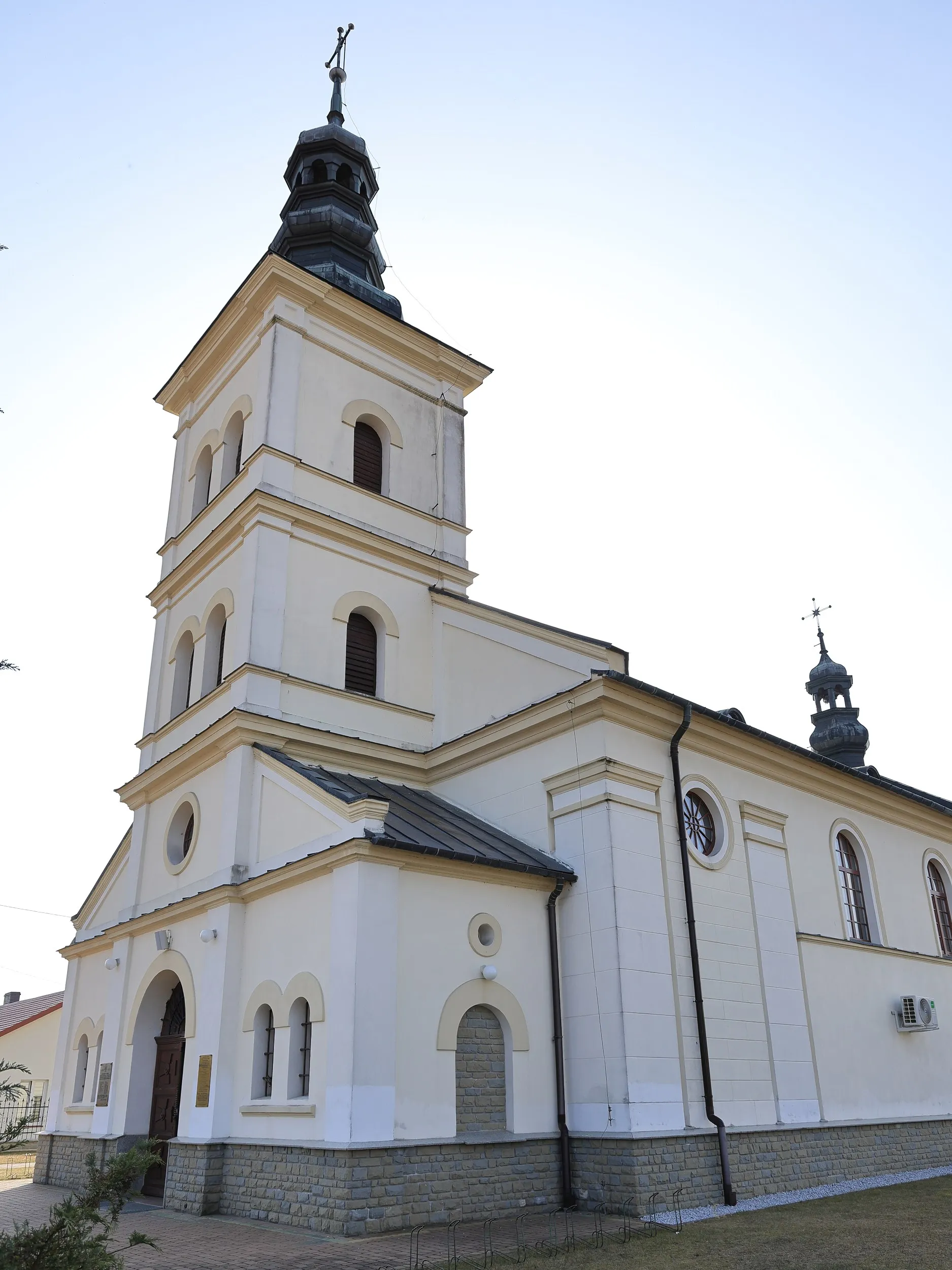 Widok kościoła w Borzykowej od strony bocznej. Jasna elewacja świątyni z wieżą, oknami i głównym wejściem.