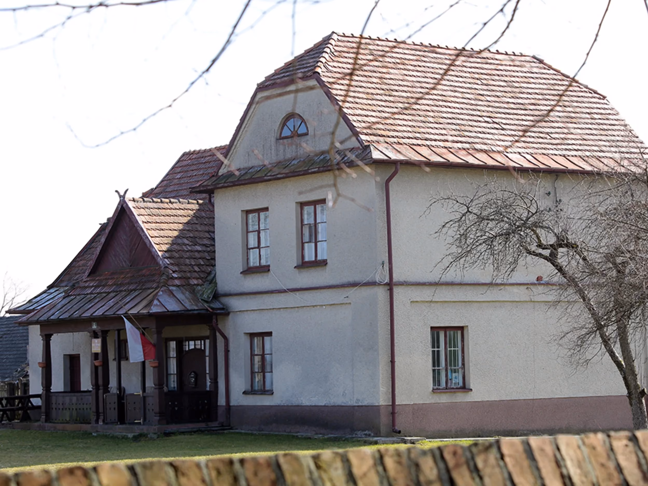 Budynek plebanii przy kościele w Maluszynie. Dwukondygnacyjny obiekt z gankiem wejściowym i polską flagą.