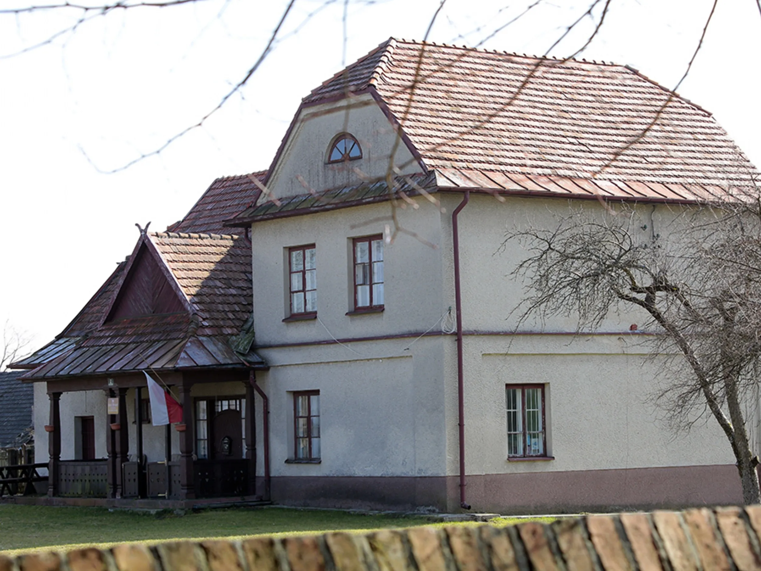 Budynek plebanii przy kościele w Maluszynie. Dwukondygnacyjny obiekt z gankiem wejściowym i polską flagą.