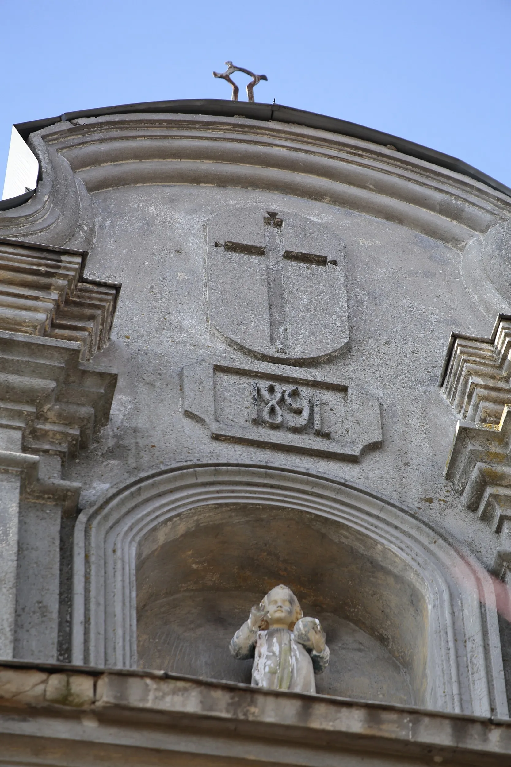 Detal elewacji kościoła w Maluszynie z wnęką, figurą Dzieciątka Jezus oraz datą 1891 umieszczoną pod krzyżem.