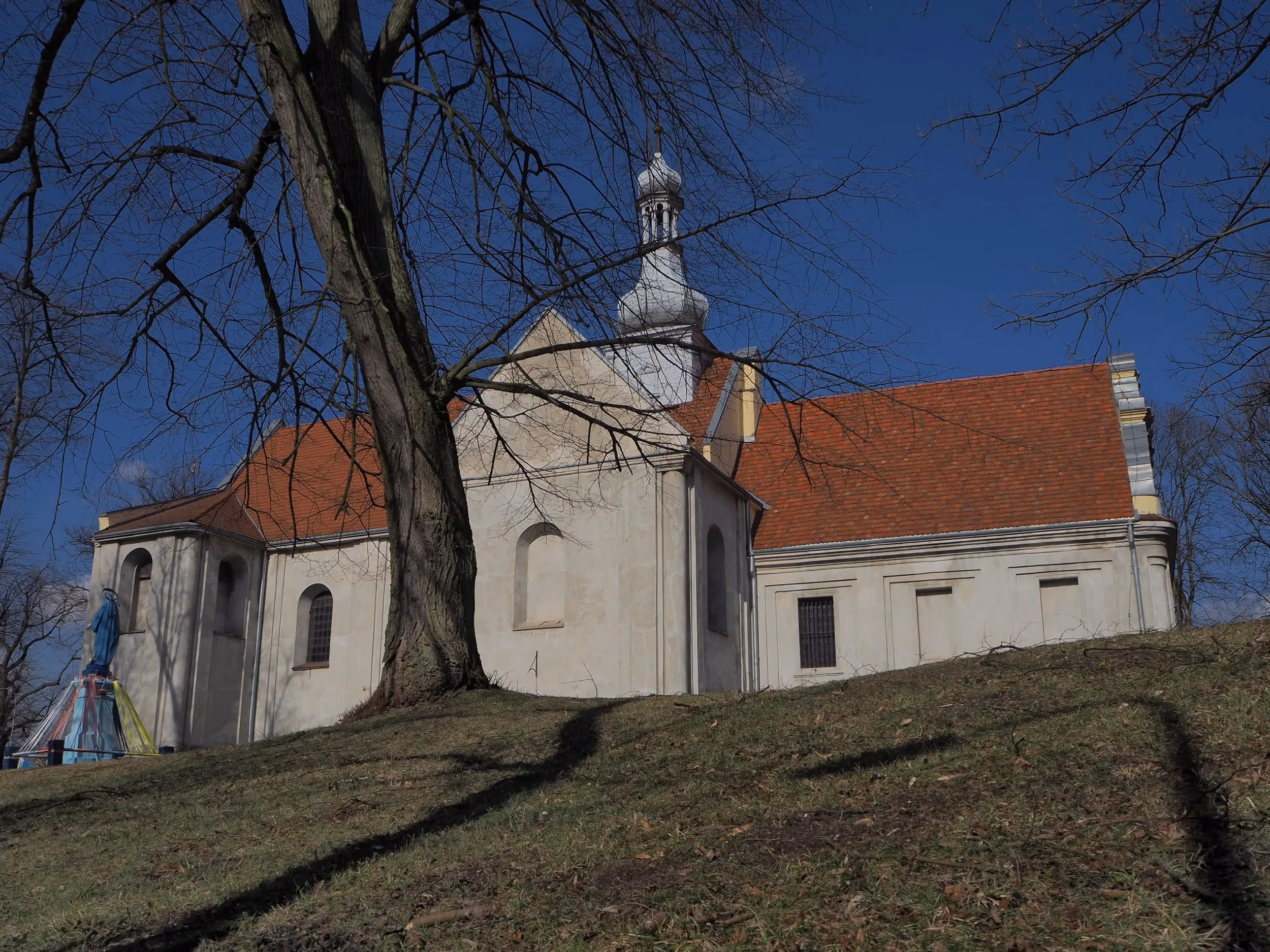Ogólny widok kościoła w Maluszynie od strony ulicy. Świątynia położona jest na niewielkim wzniesieniu wśród drzew.