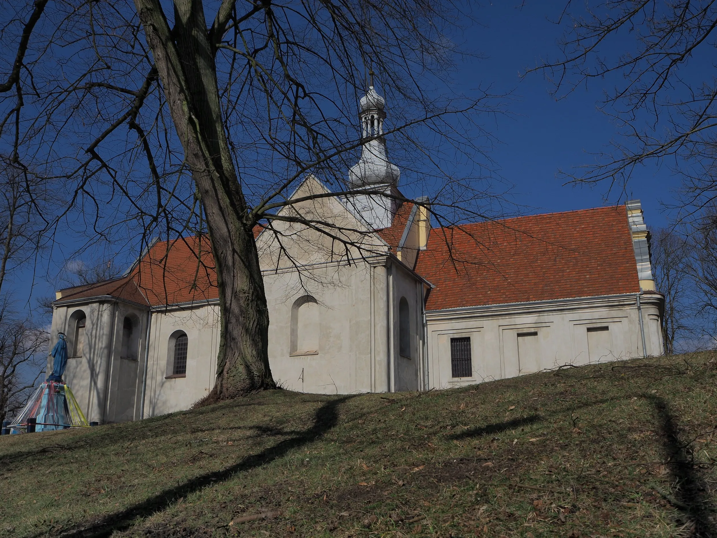 Ogólny widok kościoła w Maluszynie od strony ulicy. Świątynia położona jest na niewielkim wzniesieniu wśród drzew.