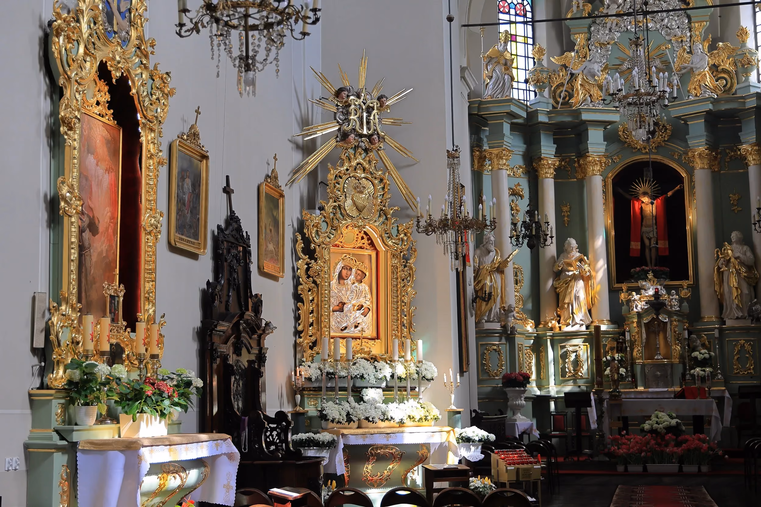 Boczna część wnętrza kościoła przy klasztorze franciszkanów w Radomsku z ołtarzem Matki Bożej, złoconymi dekoracjami i świecami.