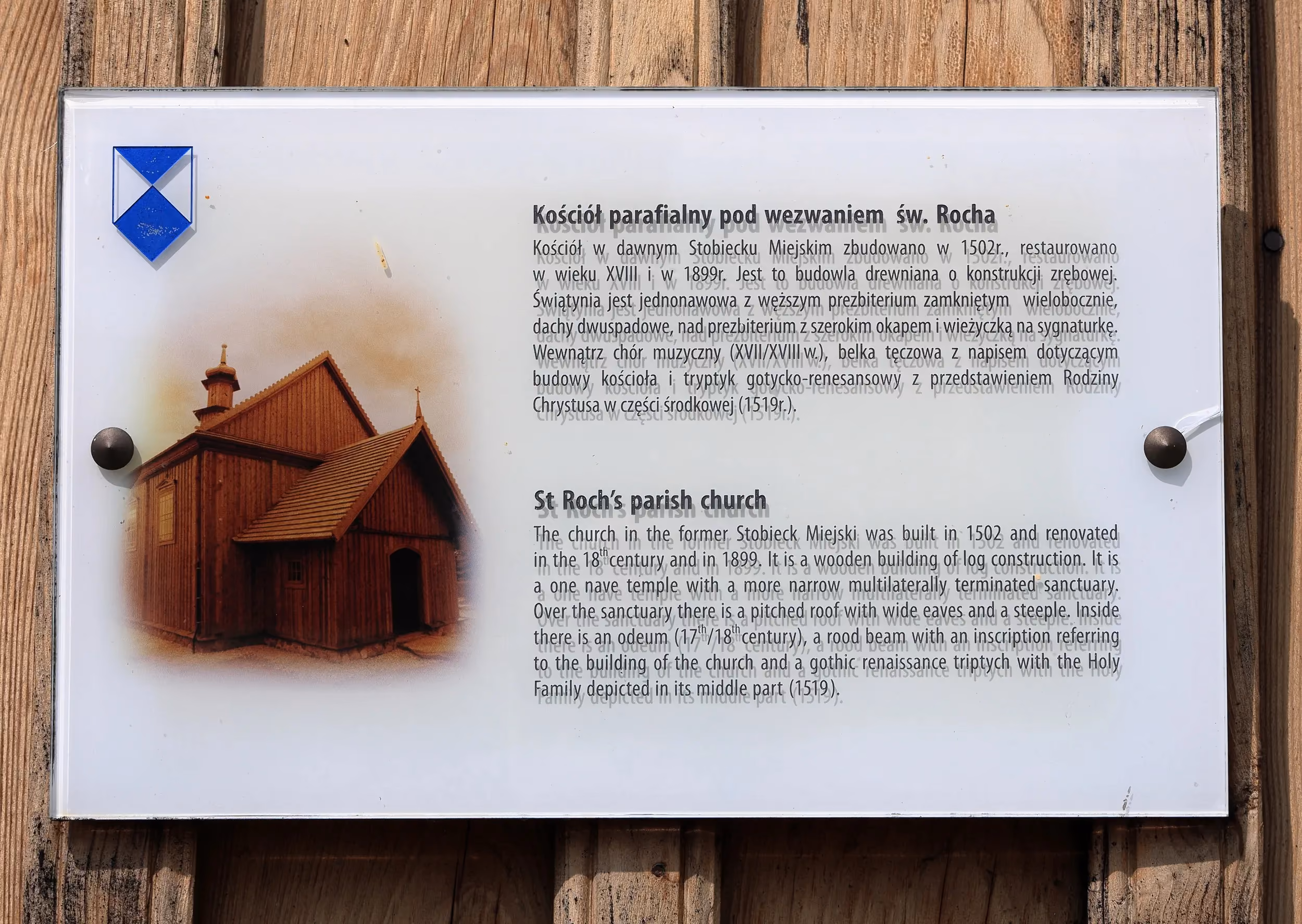 Tablica informacyjna przy kościele św. Rocha w Radomsku zawierająca opis historii zabytkowej świątyni w języku polskim i angielskim.