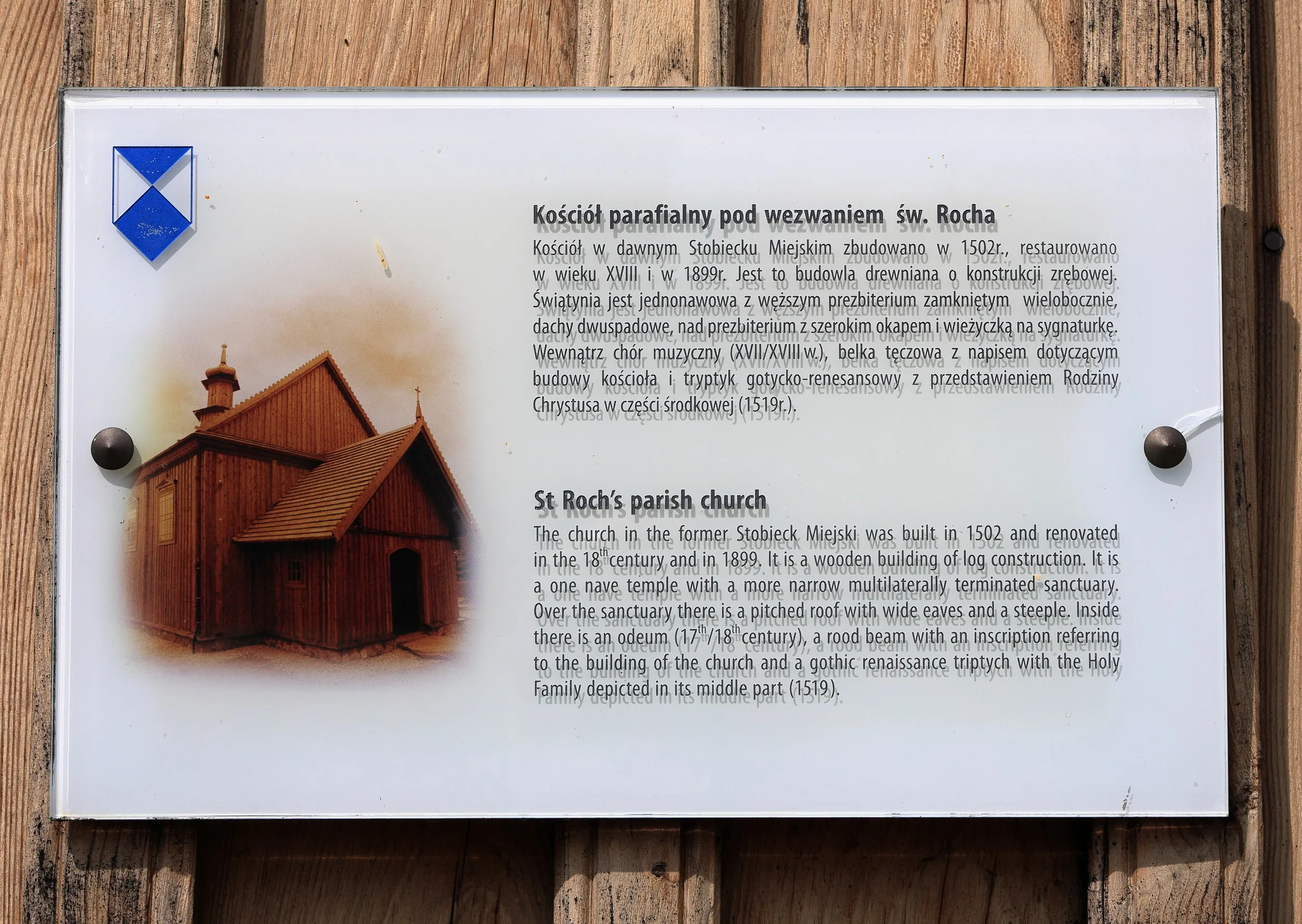 Tablica informacyjna przy kościele św. Rocha w Radomsku zawierająca opis historii zabytkowej świątyni w języku polskim i angielskim.