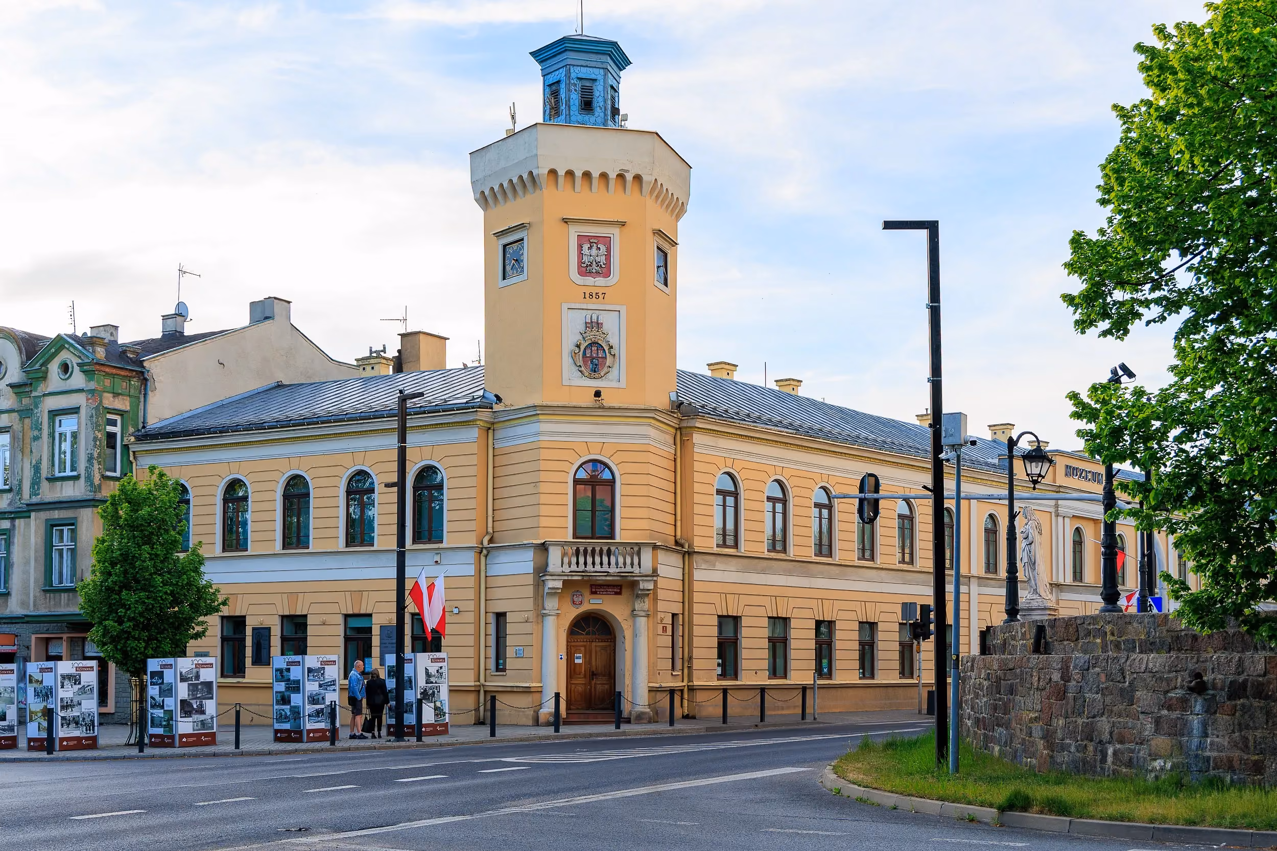 Front zabytkowego ratusza w Radomsku z centralnie usytuowaną wieżą. Przed budynkiem znajdują się flagi oraz plansze wystawowe.