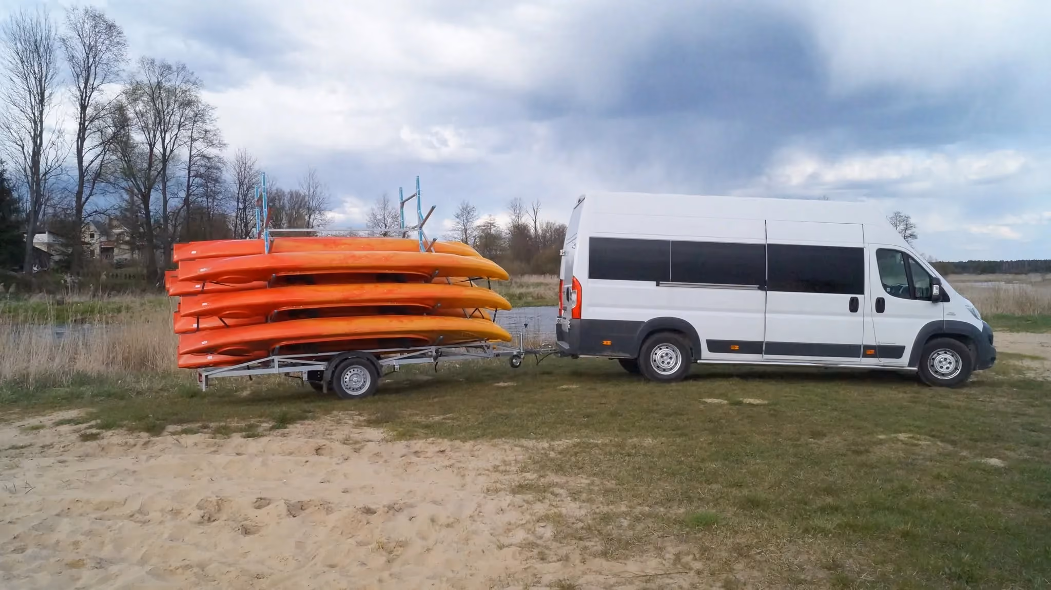 Bus z przyczepą załadowaną kolorowymi kajakami przygotowanymi do organizacji spływów kajakowych na Pilicy.