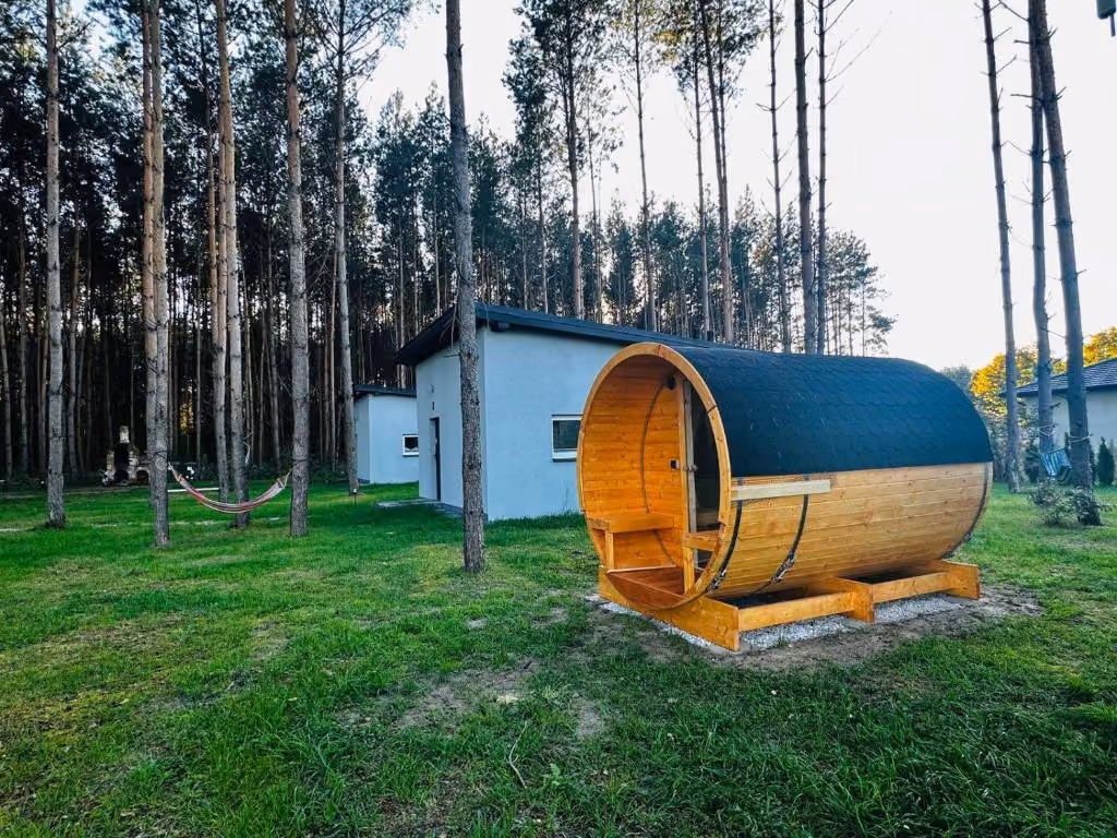 Drewniana sauna w kształcie beczki położona przy nowoczesnych domkach wypoczynkowych w sosnowym lesie.