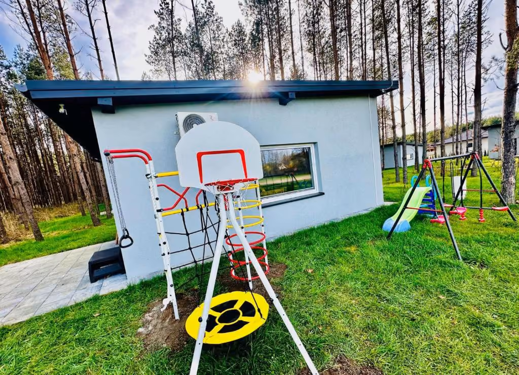 Plac zabaw z huśtawkami, drabinką i koszem do koszykówki na terenie obiektu.