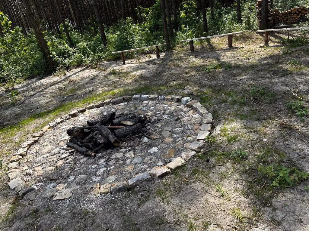 Palenisko otoczone kamieniami i drewnianymi ławkami, przeznaczone do wspólnych spotkań przy ognisku.