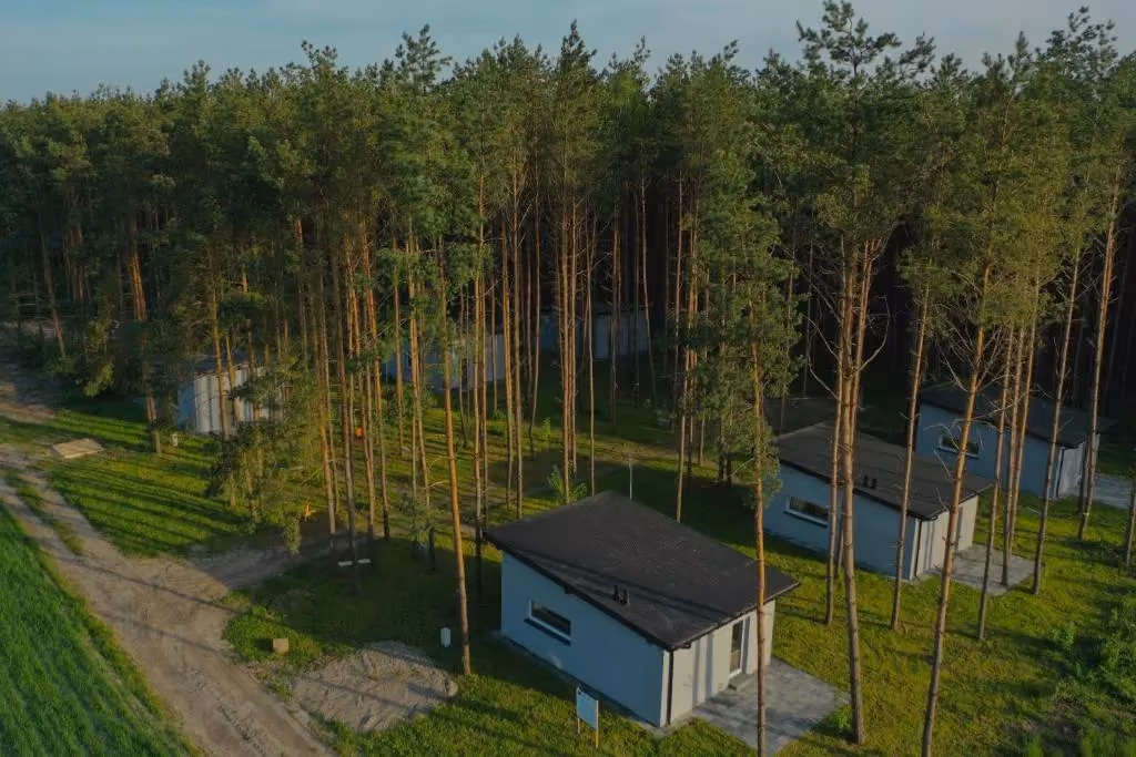 Widok z lotu ptaka na nowoczesne domki wypoczynkowe położone wśród sosnowego lasu.