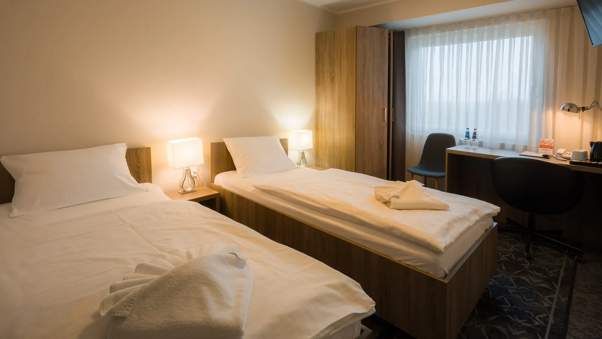 Jasny pokój dwuosobowy w Hotelu Porto z dwoma pojedynczymi łóżkami, biurkiem oraz dużym oknem zapewniającym naturalne światło.