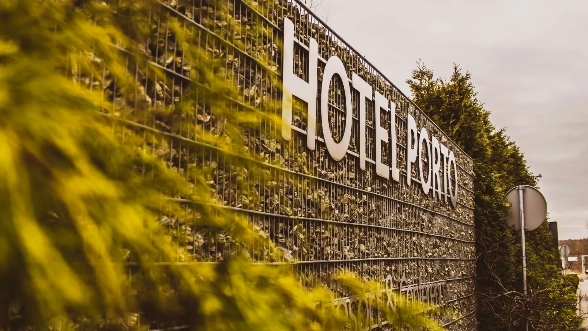 Logo Hotelu Porto umieszczone na nowoczesnym ogrodzeniu z kamiennym wypełnieniem przy wjeździe na teren obiektu.