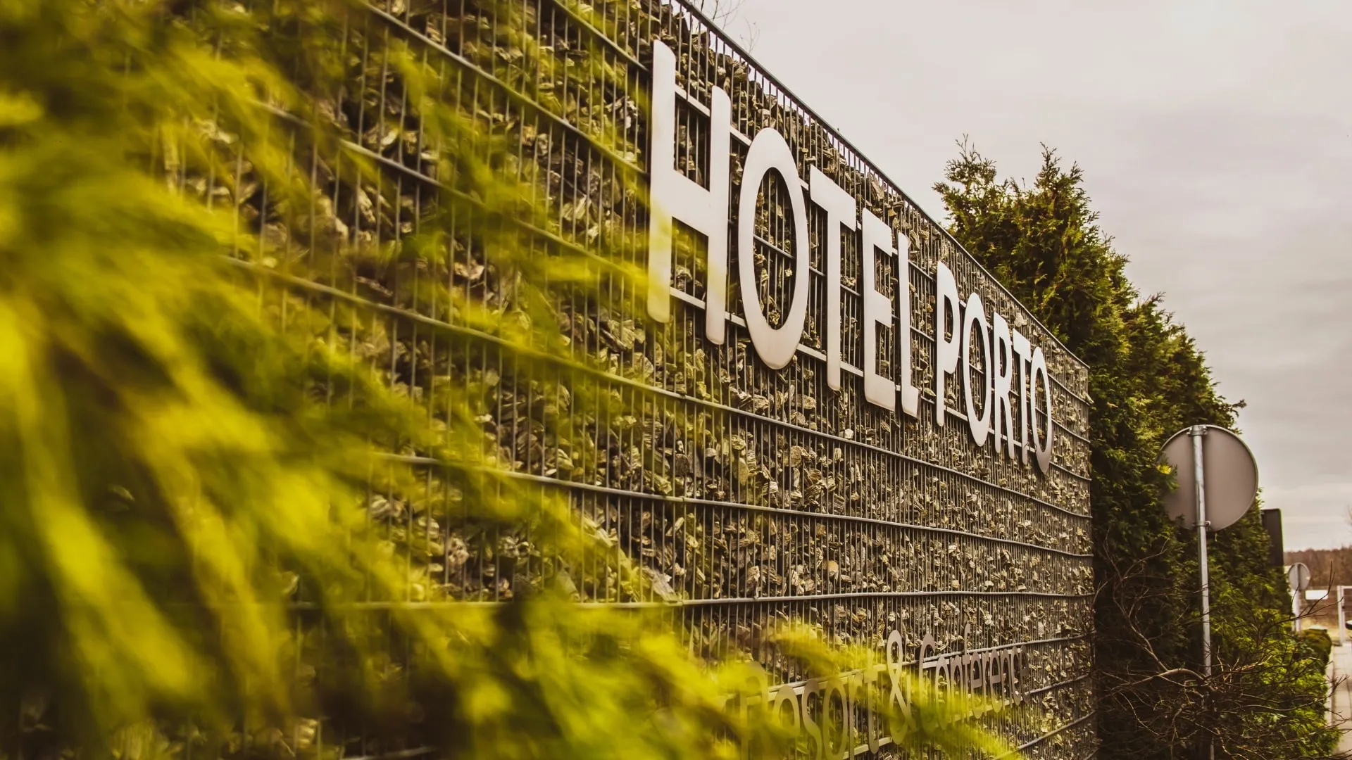 Logo Hotelu Porto umieszczone na nowoczesnym ogrodzeniu z kamiennym wypełnieniem przy wjeździe na teren obiektu.