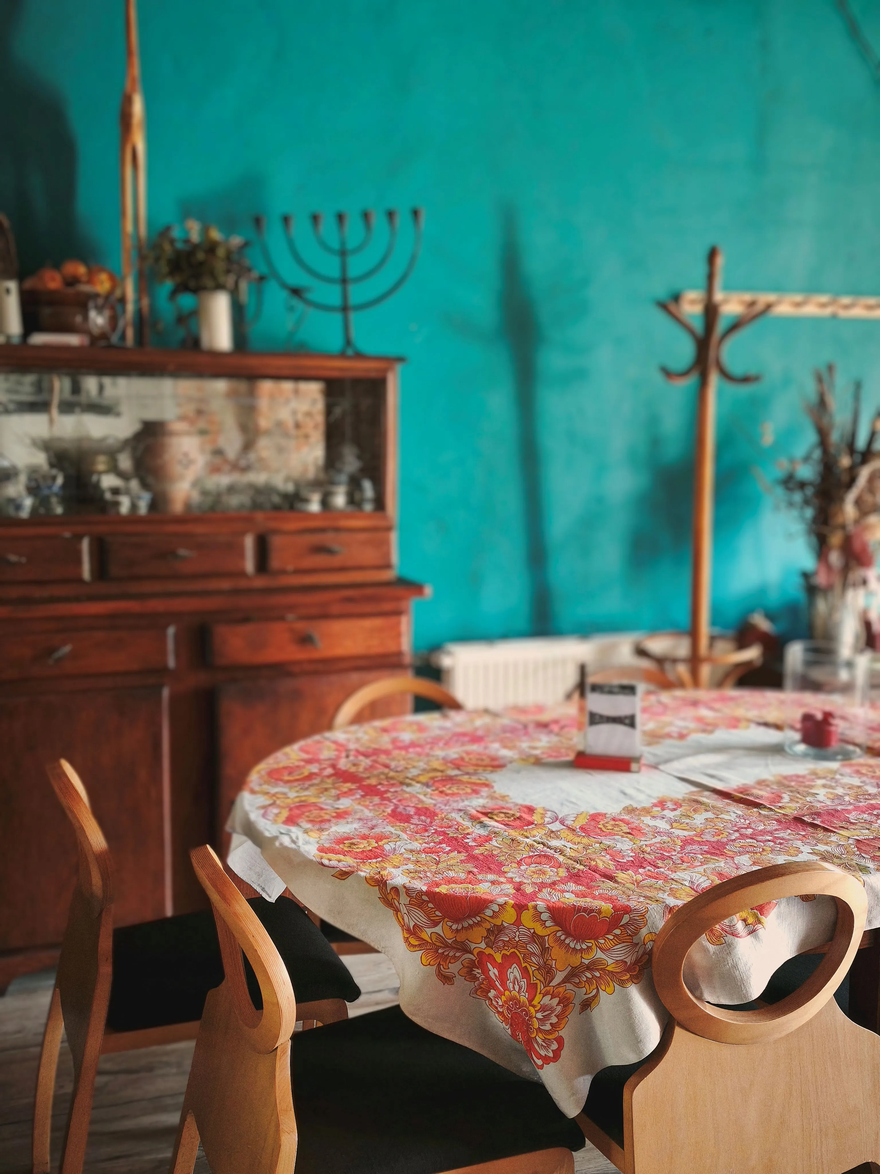 Przytulna sala restauracyjna Baru Strzecha z drewnianymi meblami, kolorowym obrusem w folkowe wzory oraz stylowymi elementami dekoracyjnymi na tle turkusowej ściany.