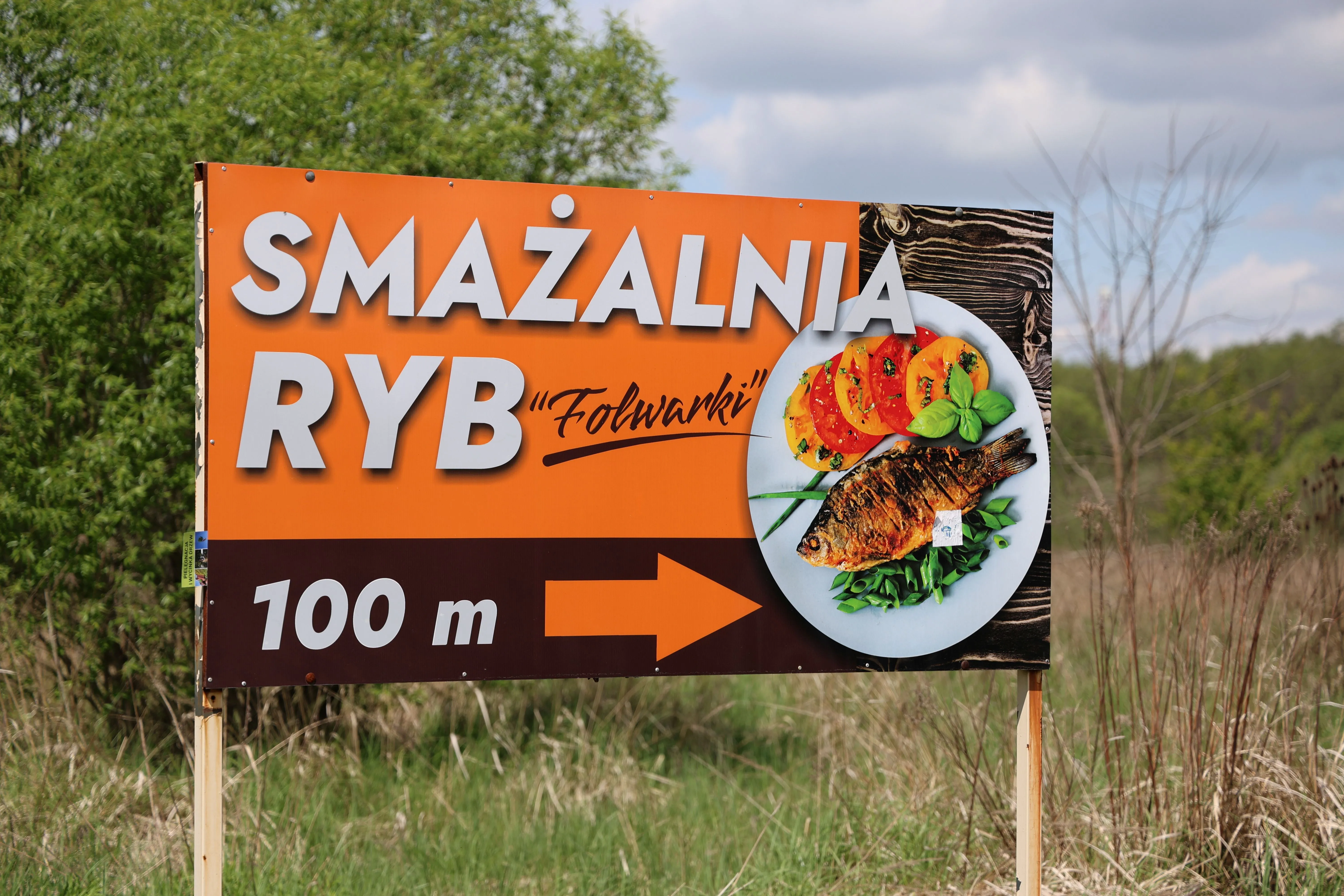 Tablica kierunkowa prowadząca do Smażalni Ryb Folwarki z informacją o lokalizacji obiektu.