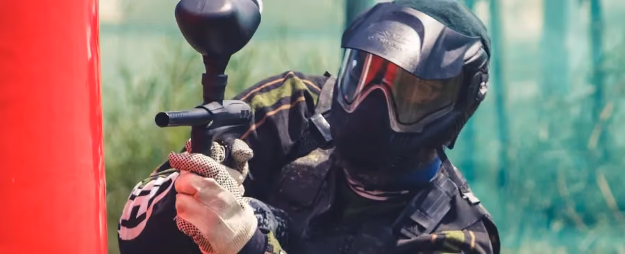Uczestnik gry paintballowej w pełnym wyposażeniu ochronnym ukryty za przeszkodą podczas rozgrywki na terenie Rancza u Biskupa.