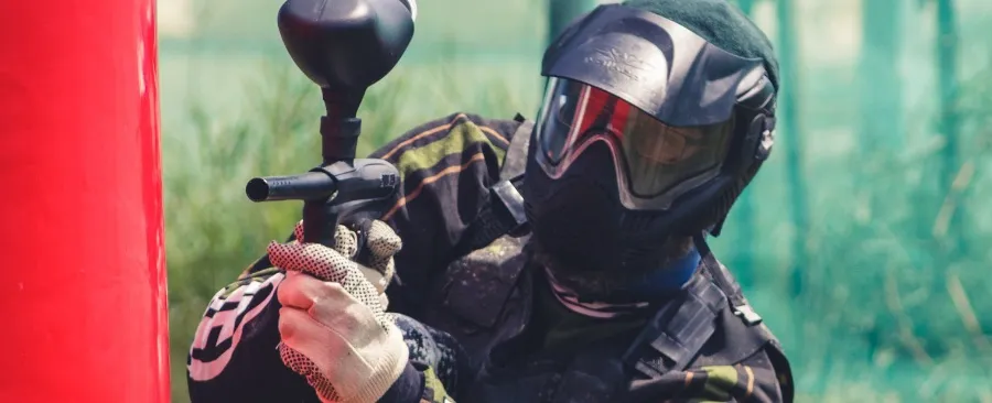 Uczestnik gry paintballowej w pełnym wyposażeniu ochronnym ukryty za przeszkodą podczas rozgrywki na terenie Rancza u Biskupa.