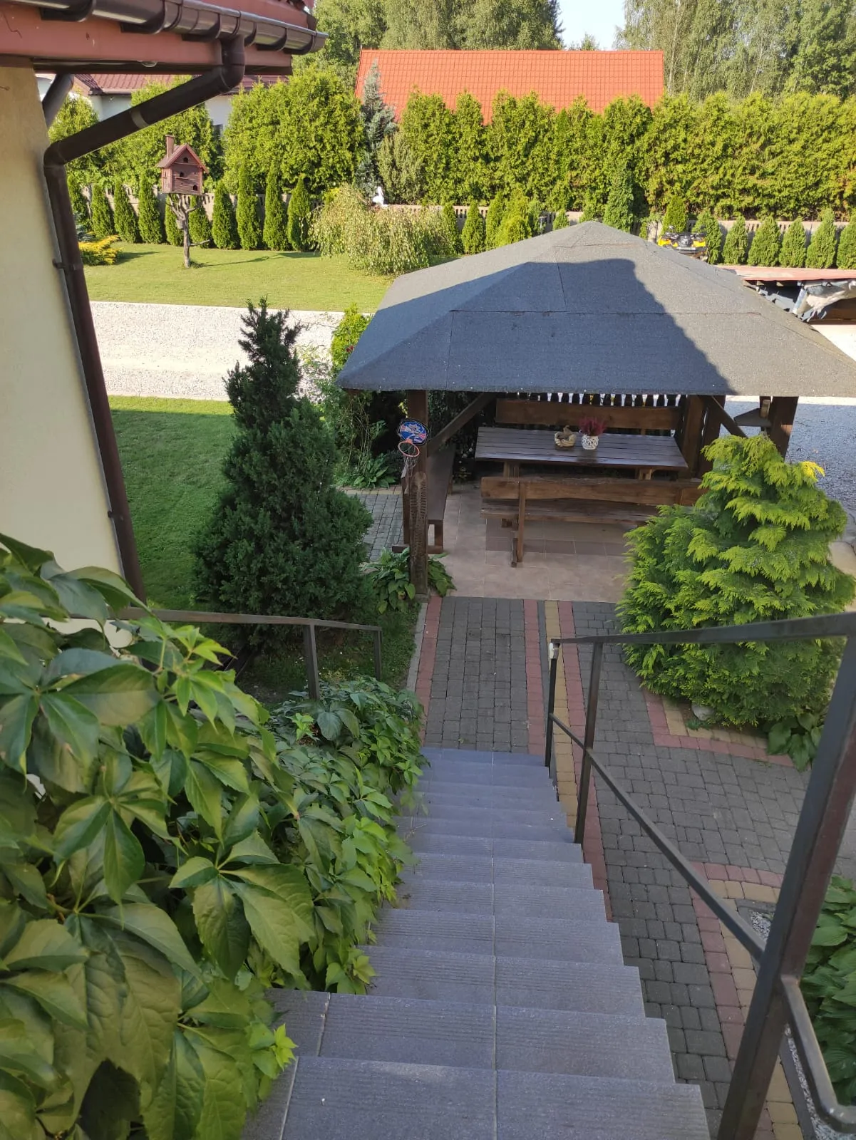 Drewniana altana ogrodowa z miejscami do biesiadowania, otoczona zadbanym ogrodem i zielenią