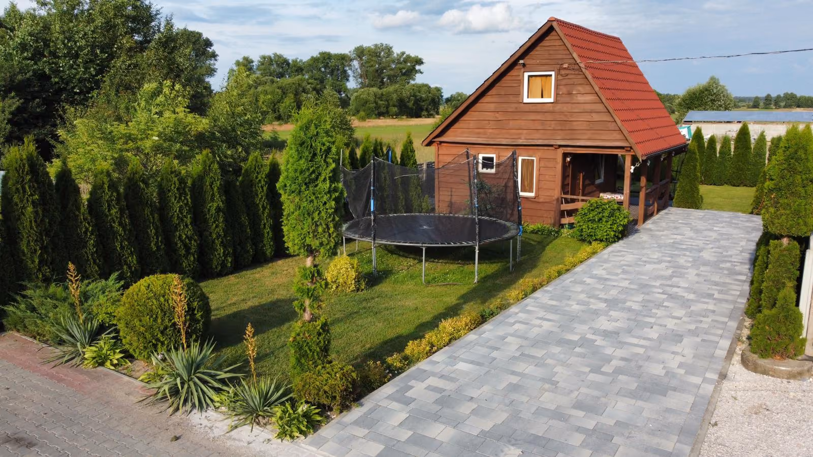 Drewniany domek otoczony zielenią z trampoliną dla dzieci i dużym ogrodem.Drewniany domek otoczony zielenią z trampoliną dla dzieci i dużym ogrodem
