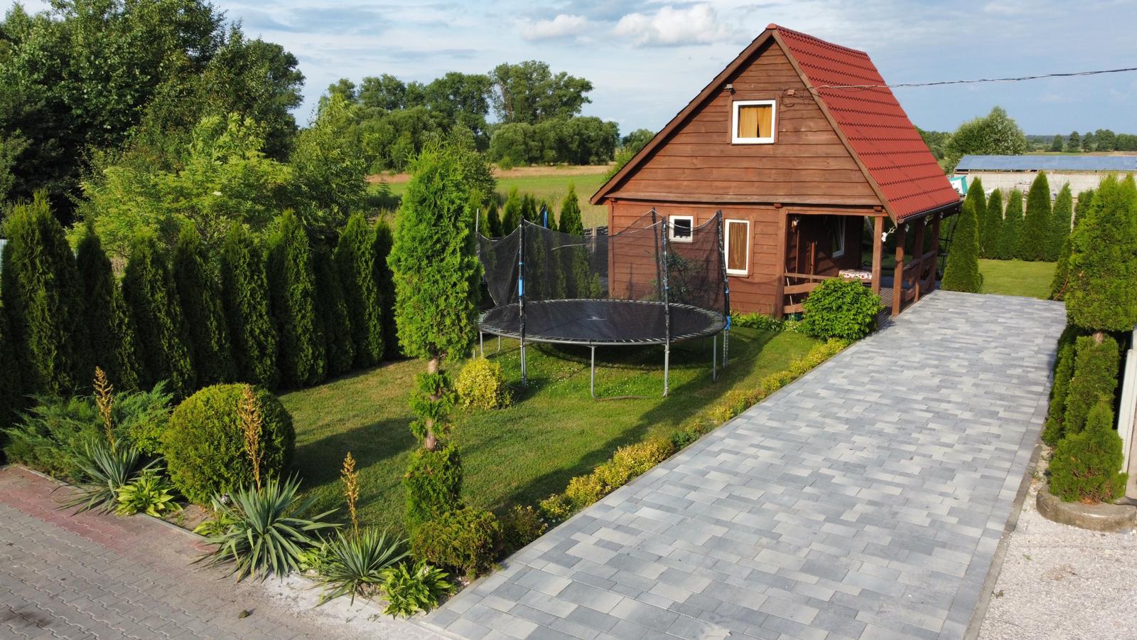 Drewniany domek otoczony zielenią z trampoliną dla dzieci i dużym ogrodem.Drewniany domek otoczony zielenią z trampoliną dla dzieci i dużym ogrodem