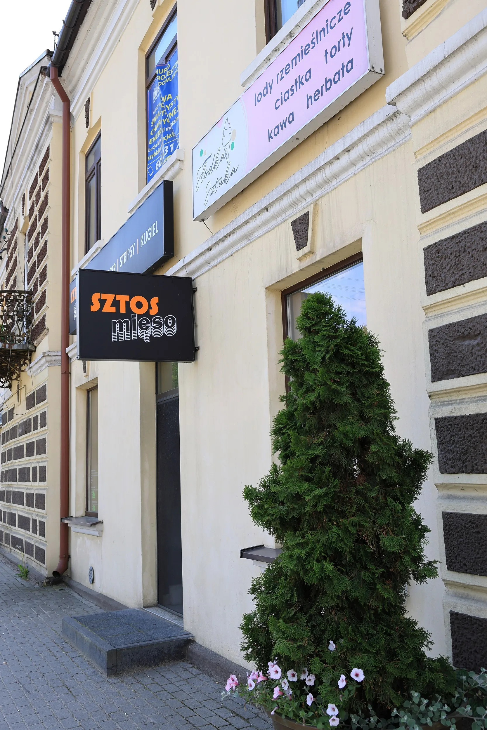 Wejście do restauracji Sztos Mięso w centrum Przedborza z widocznym szyldem lokalu i dekoracyjną zielenią.