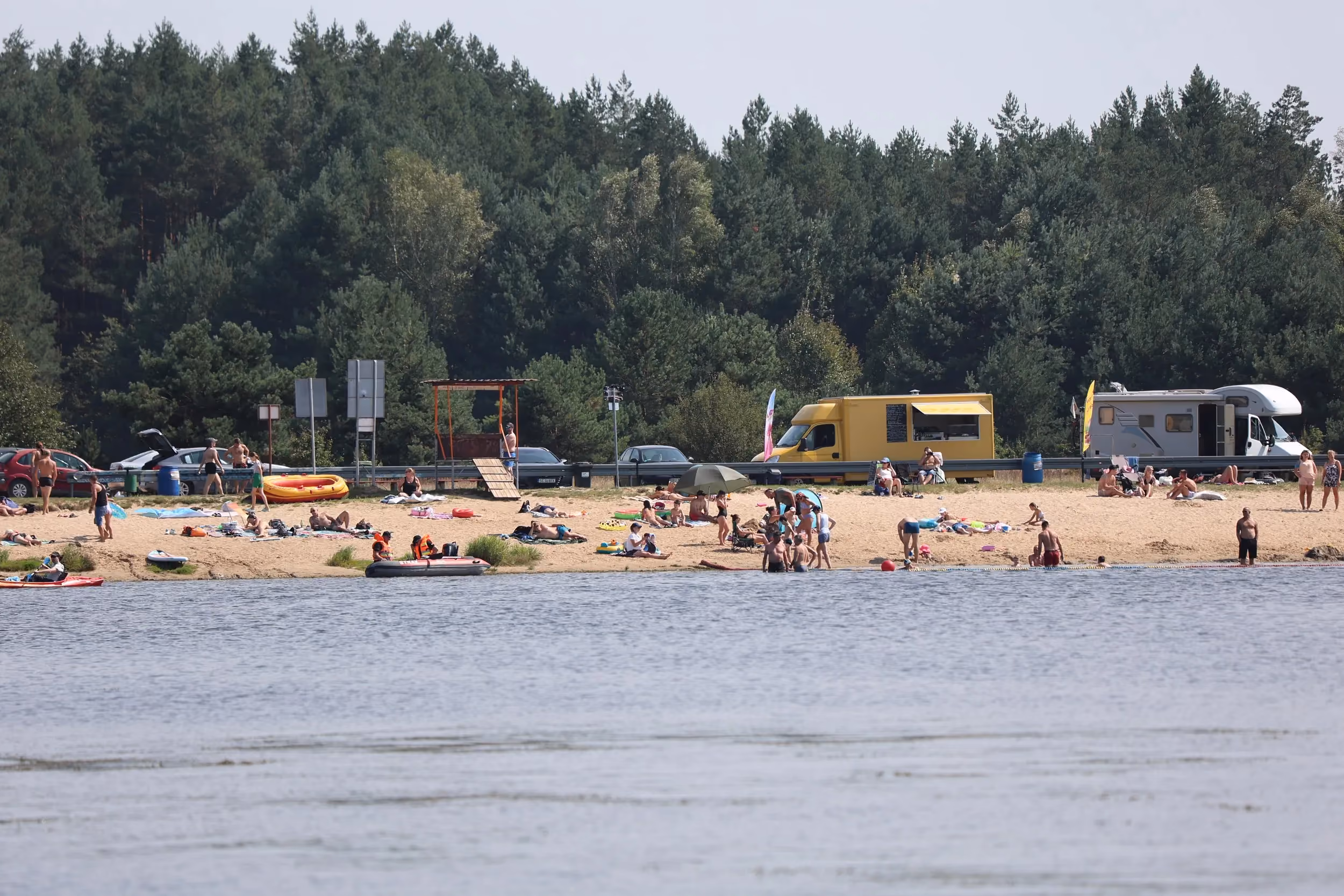 Plaża nad zbiornikiem w Zakrzówku Szlacheckim w letni dzień. Wypoczywający korzystają ze słońca, kąpieli oraz atrakcji rekreacyjnych.