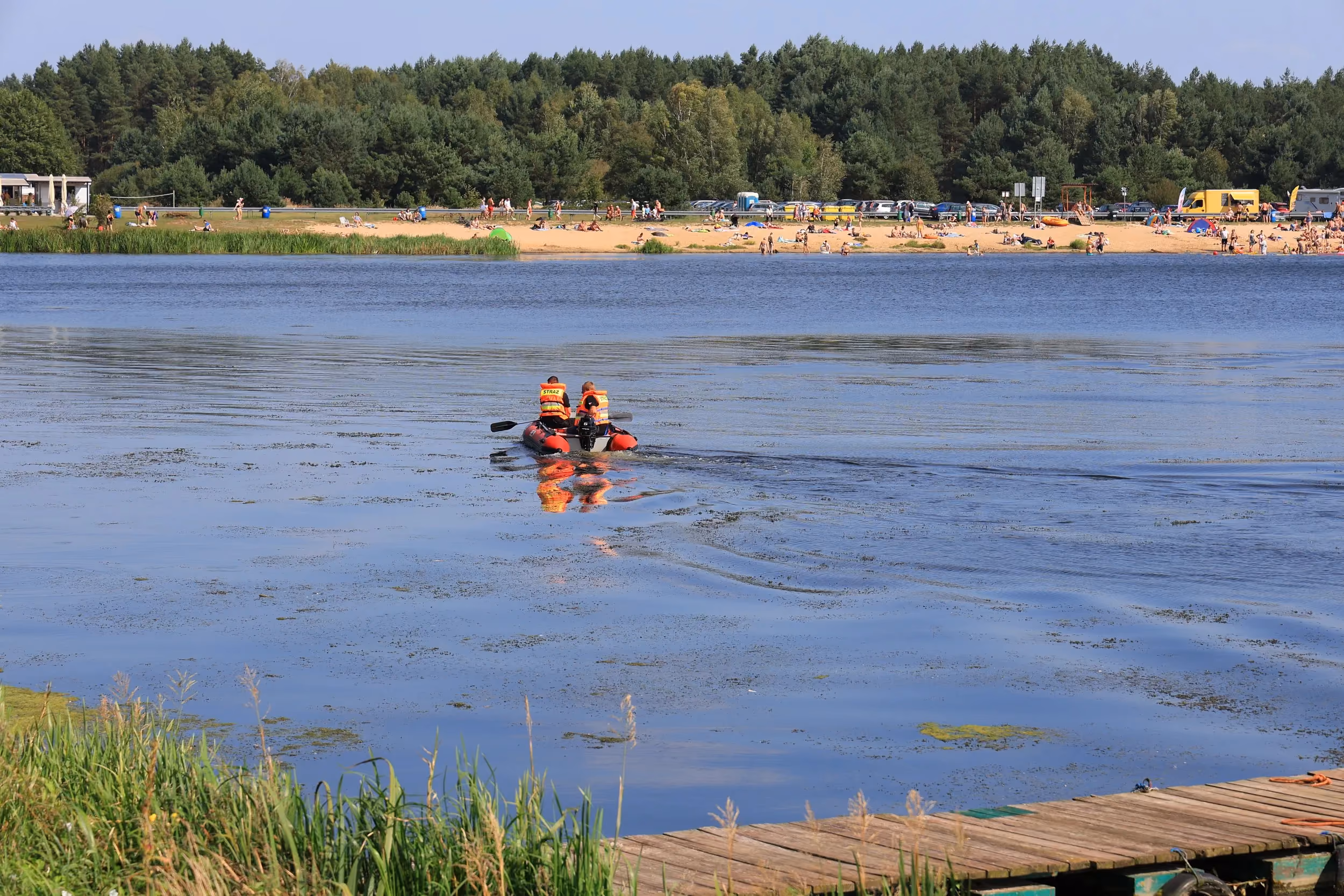 Ratownicy w pontonie patrolują zbiornik w Zakrzówku Szlacheckim. W tle widoczna jest plaża z wypoczywającymi turystami.