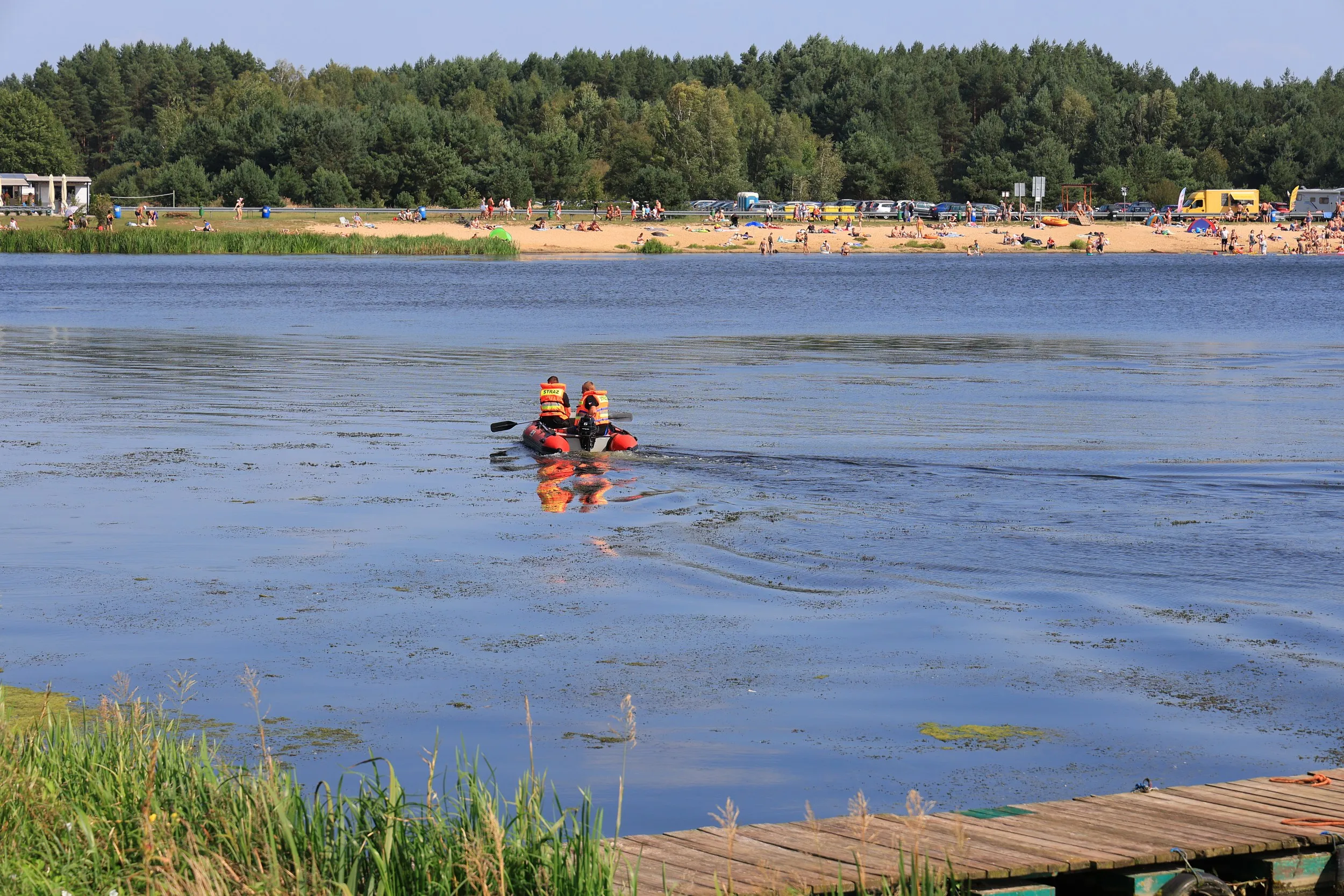 Ratownicy w pontonie patrolują zbiornik w Zakrzówku Szlacheckim. W tle widoczna jest plaża z wypoczywającymi turystami.
