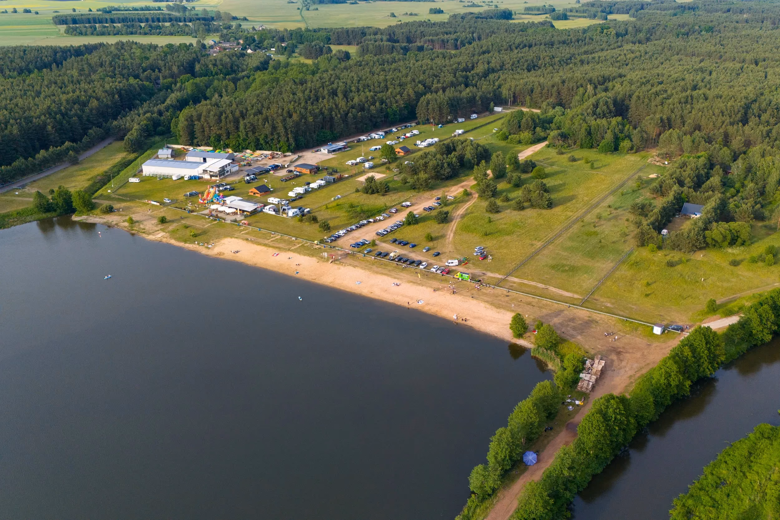 Ujęcie z drona przedstawiające plażę i ośrodek rekreacyjny nad zbiornikiem w Zakrzówku Szlacheckim. Wokół rozciągają się lasy i tereny zielone.