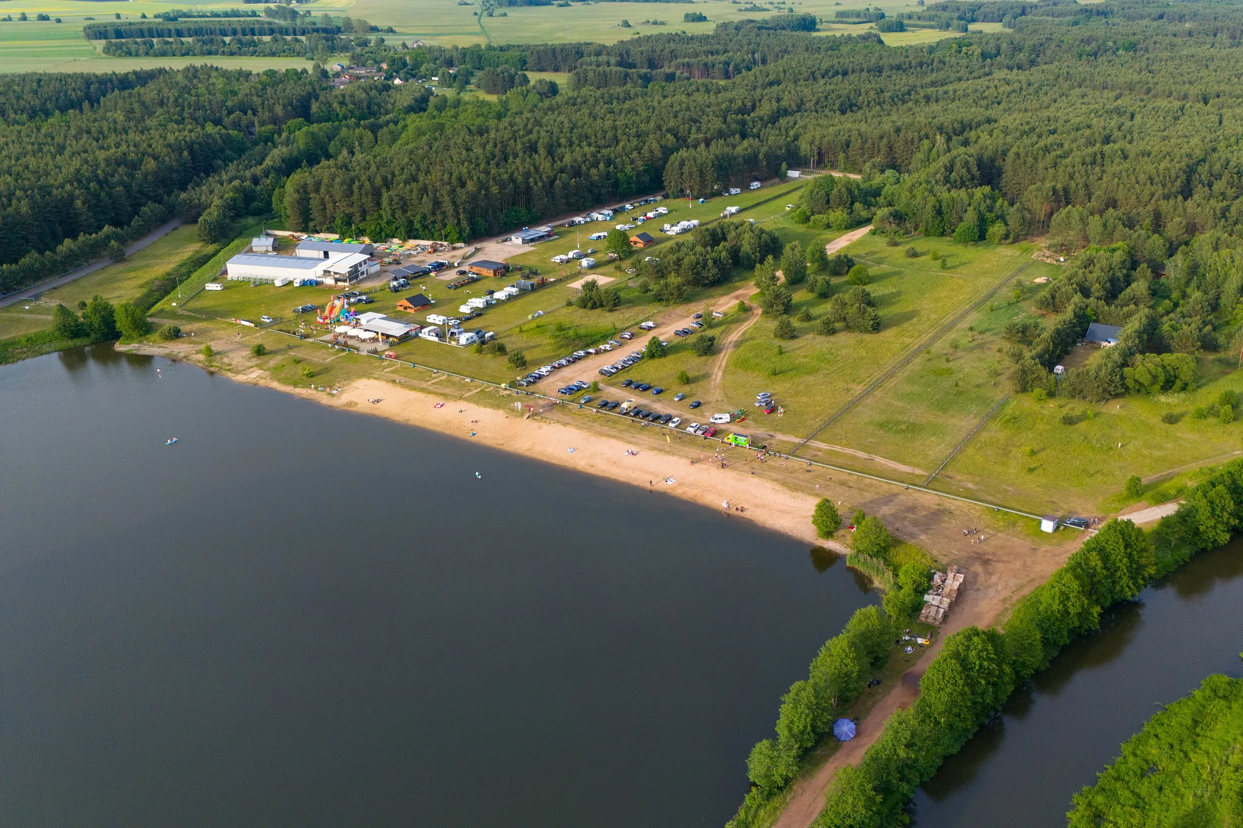 Ujęcie z drona przedstawiające plażę i ośrodek rekreacyjny nad zbiornikiem w Zakrzówku Szlacheckim. Wokół rozciągają się lasy i tereny zielone.