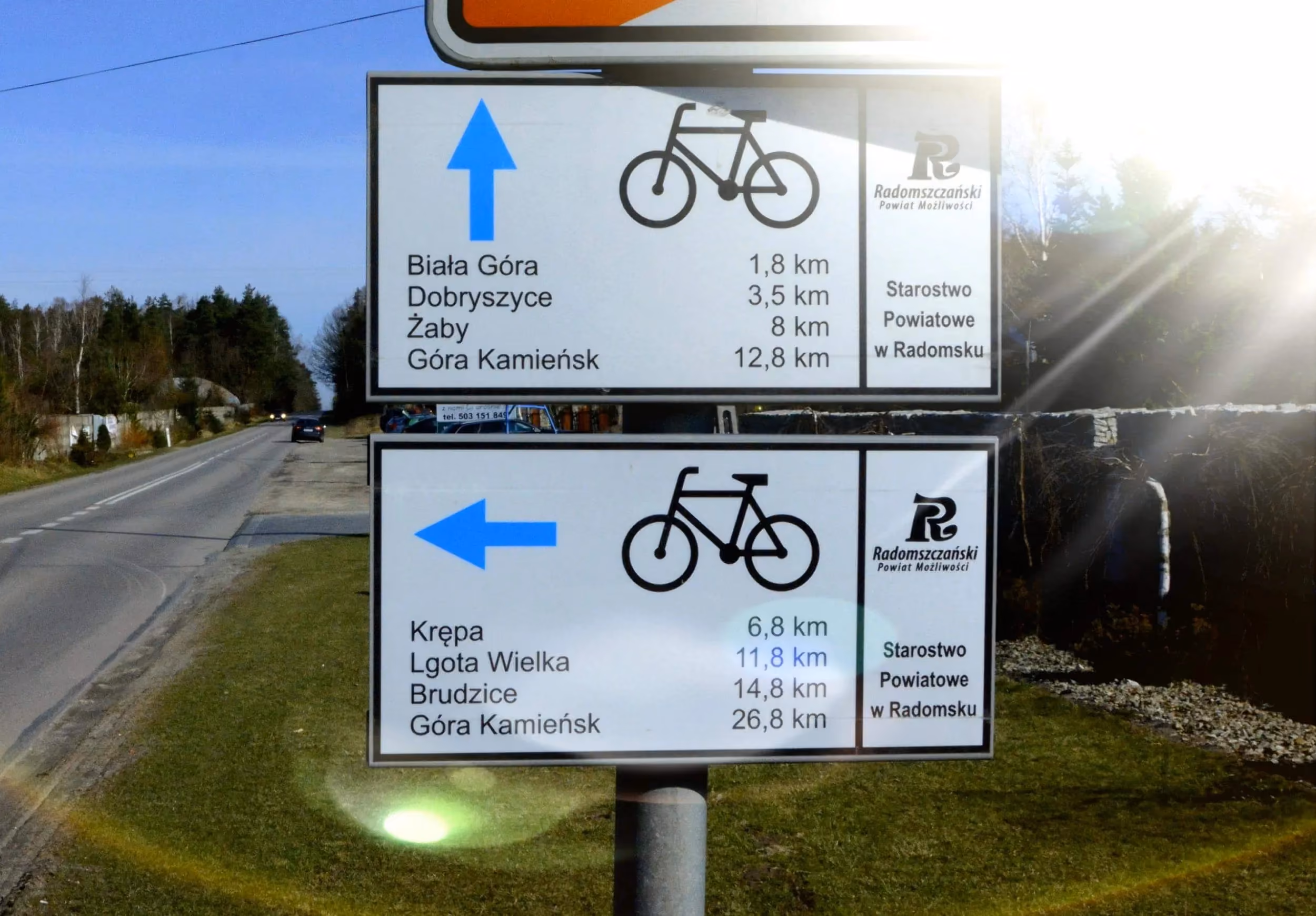 Tablice informacyjne Powiatowego Szlaku Rowerowego z odległościami do okolicznych miejscowości. Oznakowanie ustawiono przy drodze w otwartym terenie.