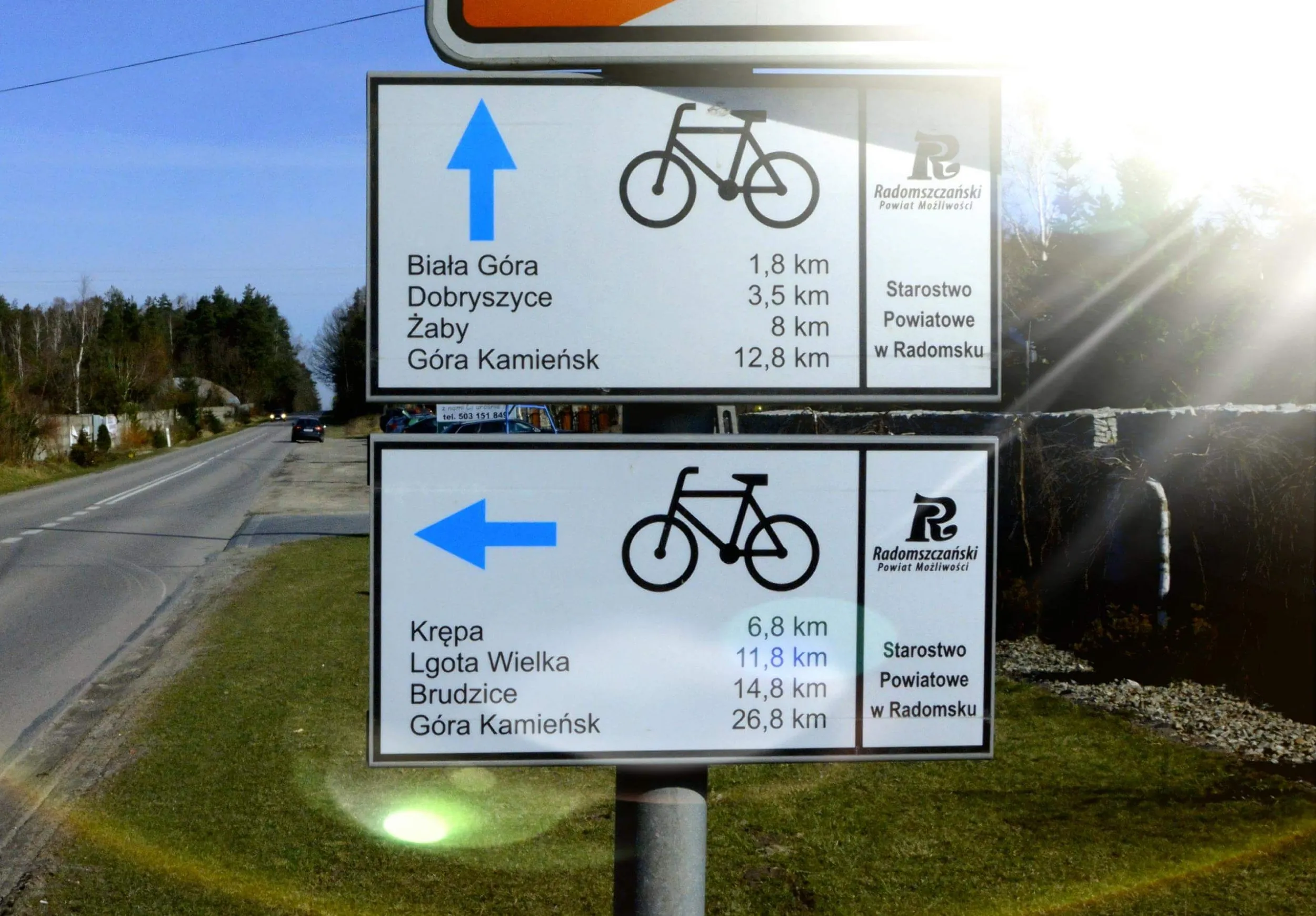 Tablice informacyjne Powiatowego Szlaku Rowerowego z odległościami do okolicznych miejscowości. Oznakowanie ustawiono przy drodze w otwartym terenie.