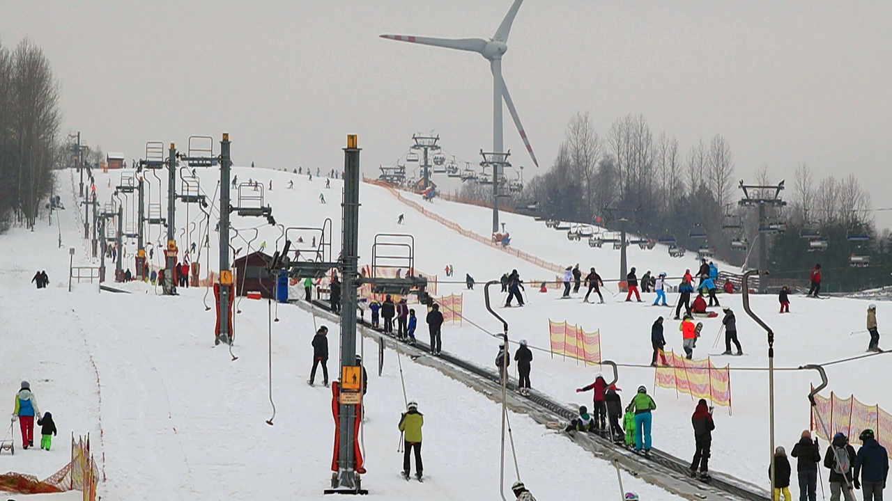 Zimowy widok na ośrodek narciarski na Górze Kamieńskiej. Na stoku i przy wyciągach przebywają liczni narciarze i snowboardziści.