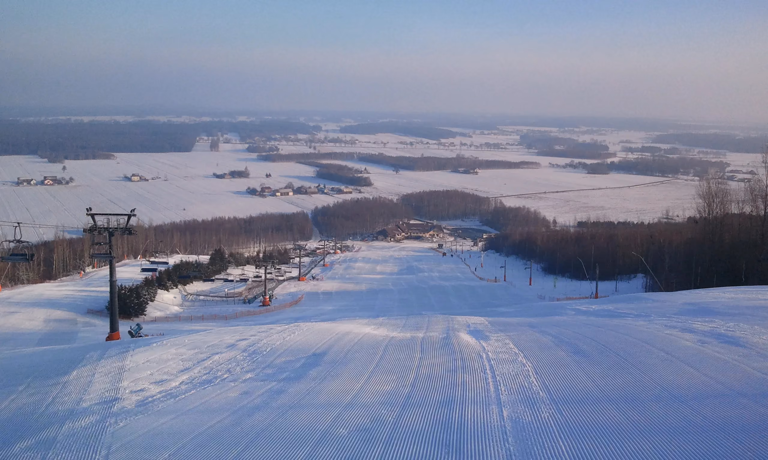 Widok ze szczytu Góry Kamieńsk na trasę narciarską i rozległą panoramę województwa łódzkiego zimą.
