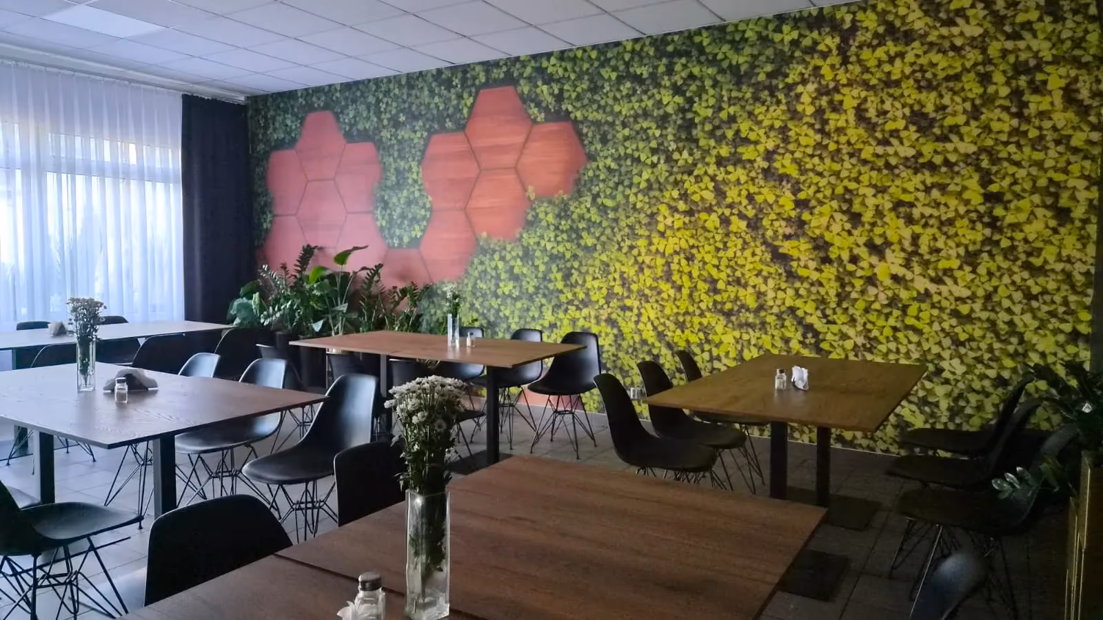Sala Bistro Pod Klonem z dekoracyjną ścianą roślinną, stolikami dla gości i przyjazną atmosferą.
