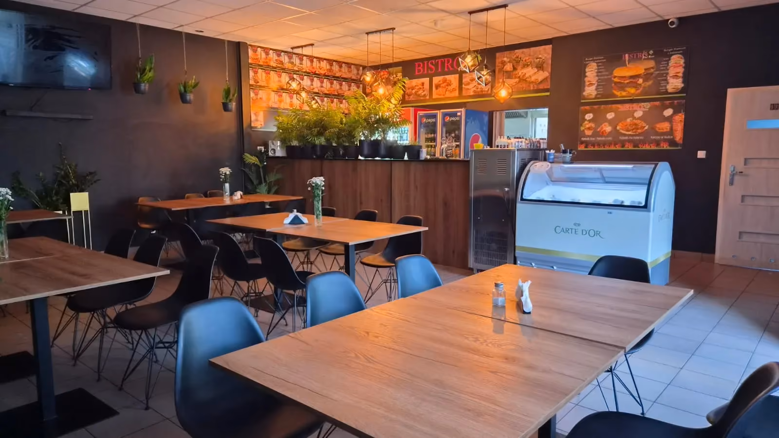 Bar i część restauracyjna Bistro Pod Klonem z nowoczesnym wyposażeniem oraz roślinnymi dekoracjami.