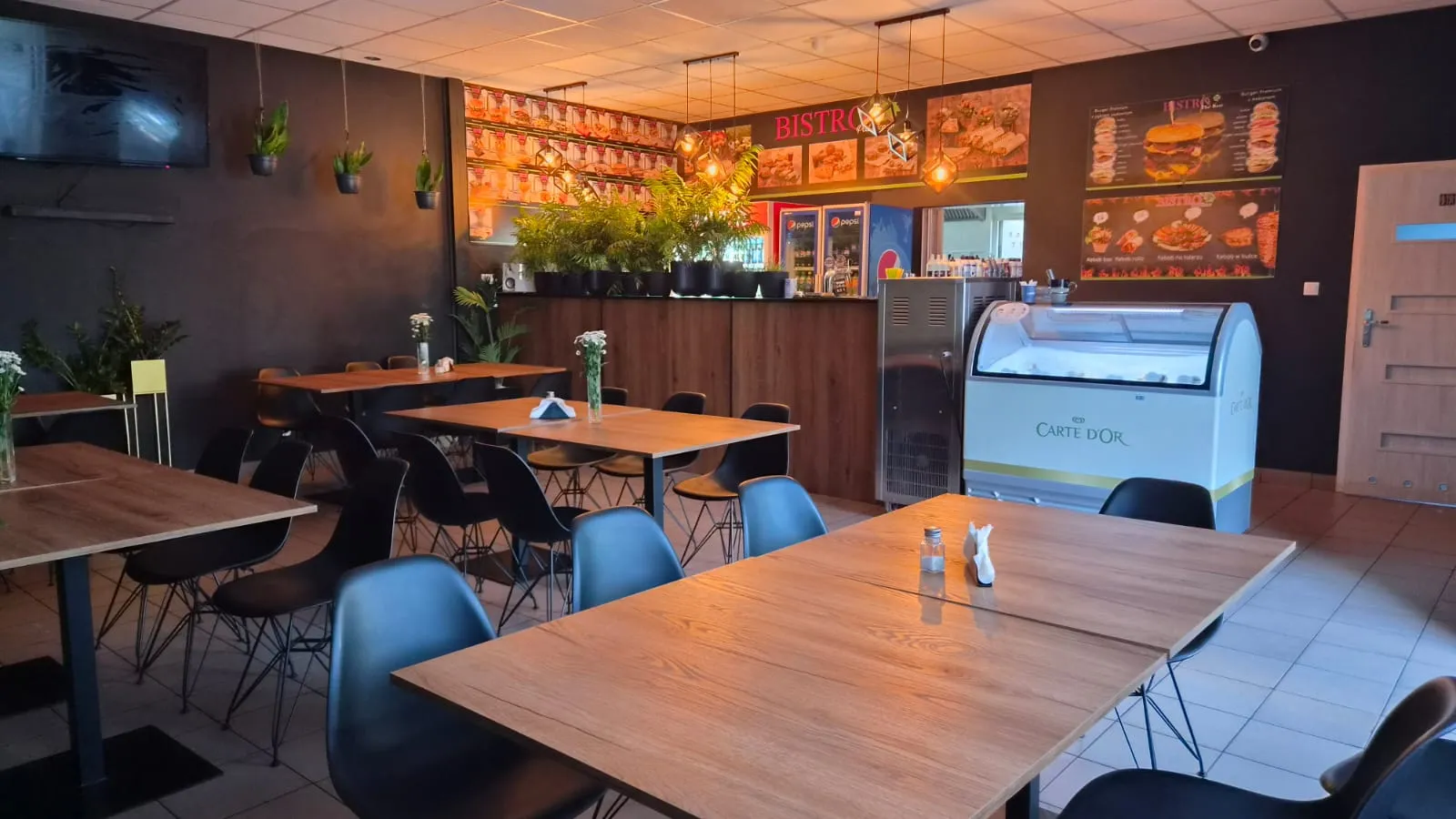 Bar i część restauracyjna Bistro Pod Klonem z nowoczesnym wyposażeniem oraz roślinnymi dekoracjami.