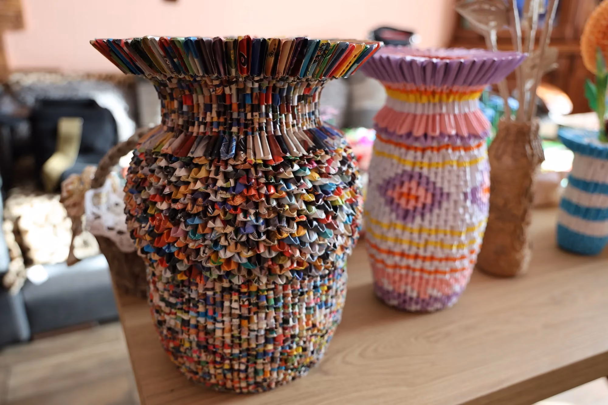 Dwa ręcznie wykonane wazony techniką origami modułowego stojące na drewnianym blacie; wazon po lewej jest wielobarwny, po prawej biało-różowo-fioletowy