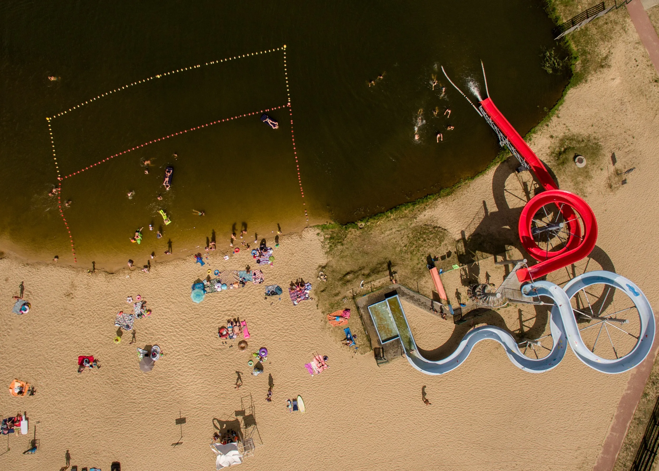Widok z góry na kąpielisko w Przedborzu z plażą, kąpiącymi się osobami, wyznaczoną strefą pływania i zjeżdżalniami.