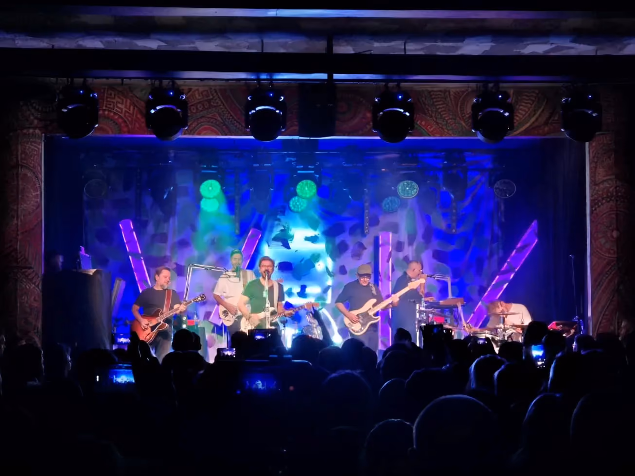 Koncert zespołu w klubie Bogart, z muzykami na scenie, kolorowym oświetleniem i publicznością przed sceną.