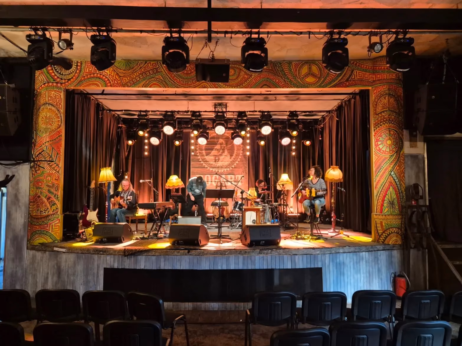 Scena klubu Bogart podczas próby lub koncertu, z muzykami, instrumentami i ciepłym oświetleniem scenicznym.