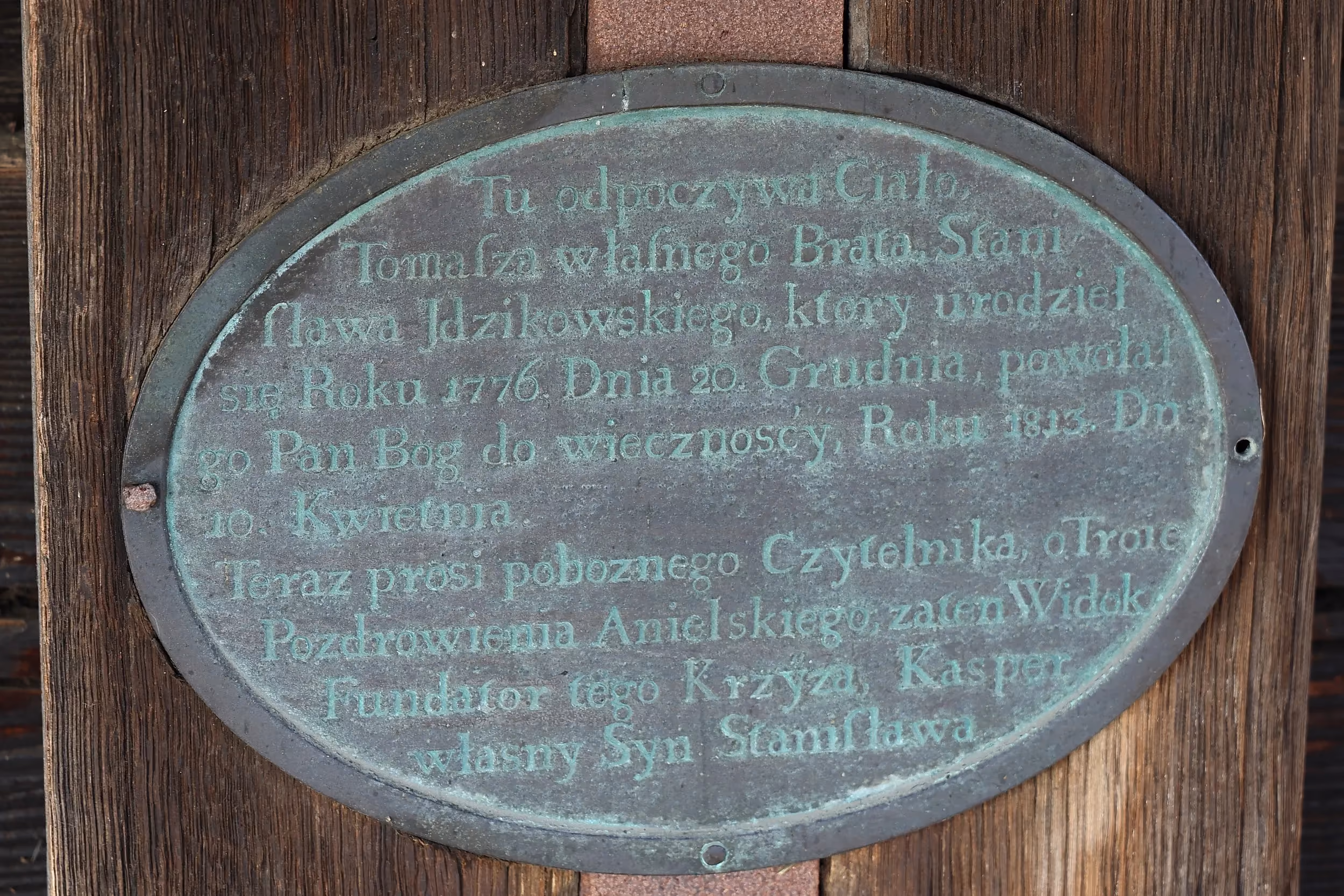 Metalowa tablica pamiątkowa z historycznym napisem, zamocowana na drewnianej ścianie zabytkowego obiektu.