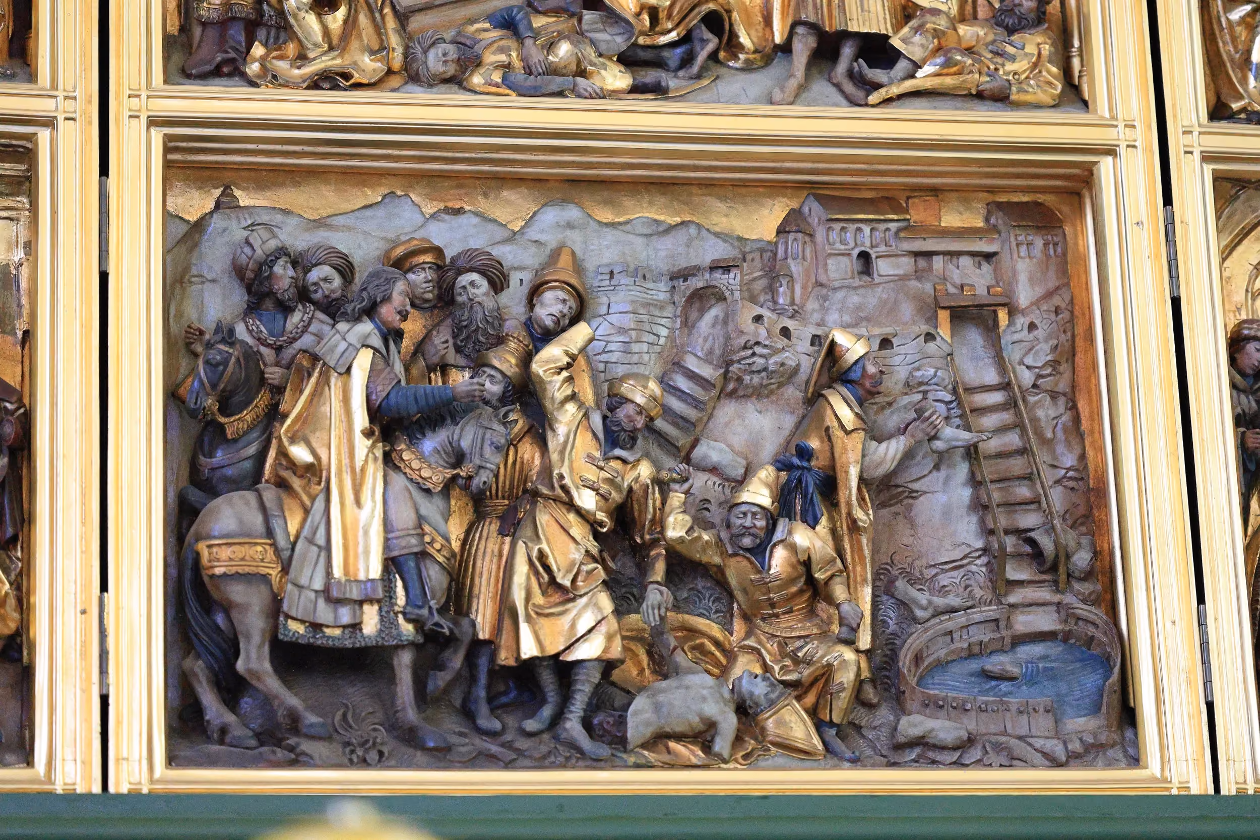 Fragment gotyckiego retabulum z reliefową sceną religijną. Wśród postaci widoczne są elementy miejskiej zabudowy, studnia oraz dekoracyjne złocenia.
