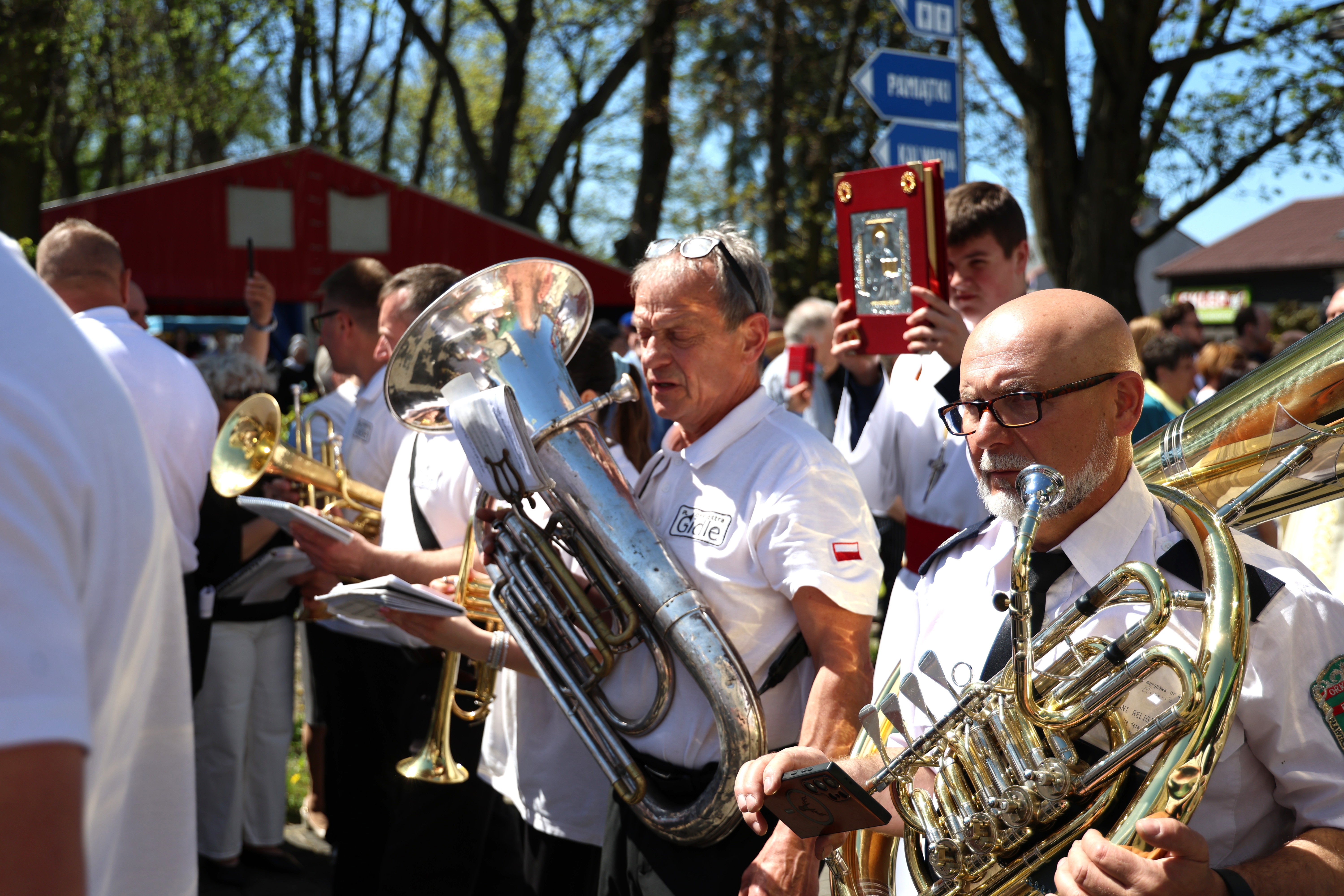Muzycy orkiestry dętej grają podczas procesji w Gidlach, wśród uczestników uroczystości niosących obraz religijny.
