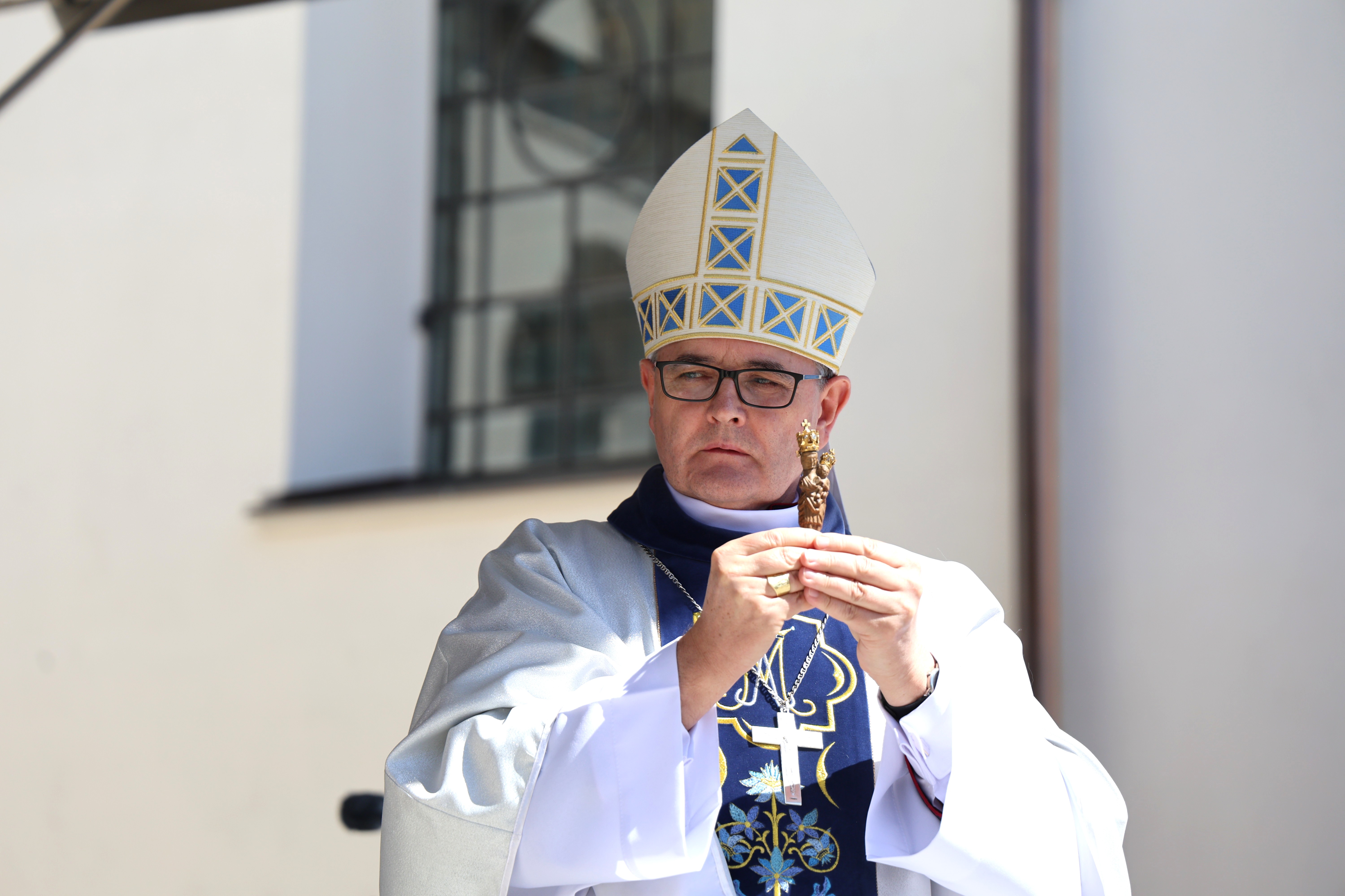 Biskup w mitrze i szatach liturgicznych trzyma w dłoniach małą figurkę Matki Bożej Gidelskiej podczas uroczystości religijnej.