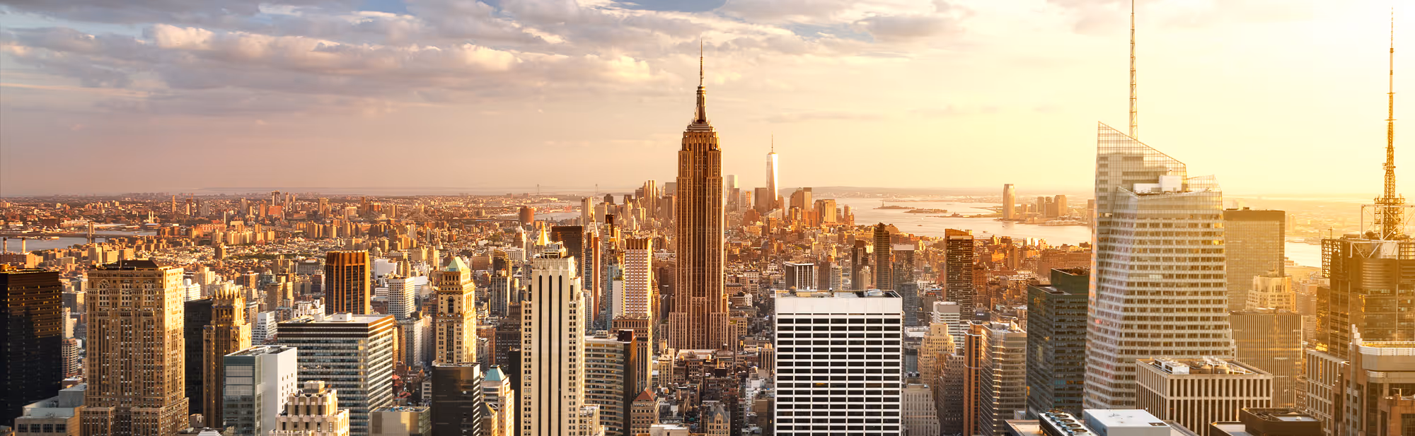 Panoramic view of New York City skyline at sunset with the Empire State Building prominently in the center.