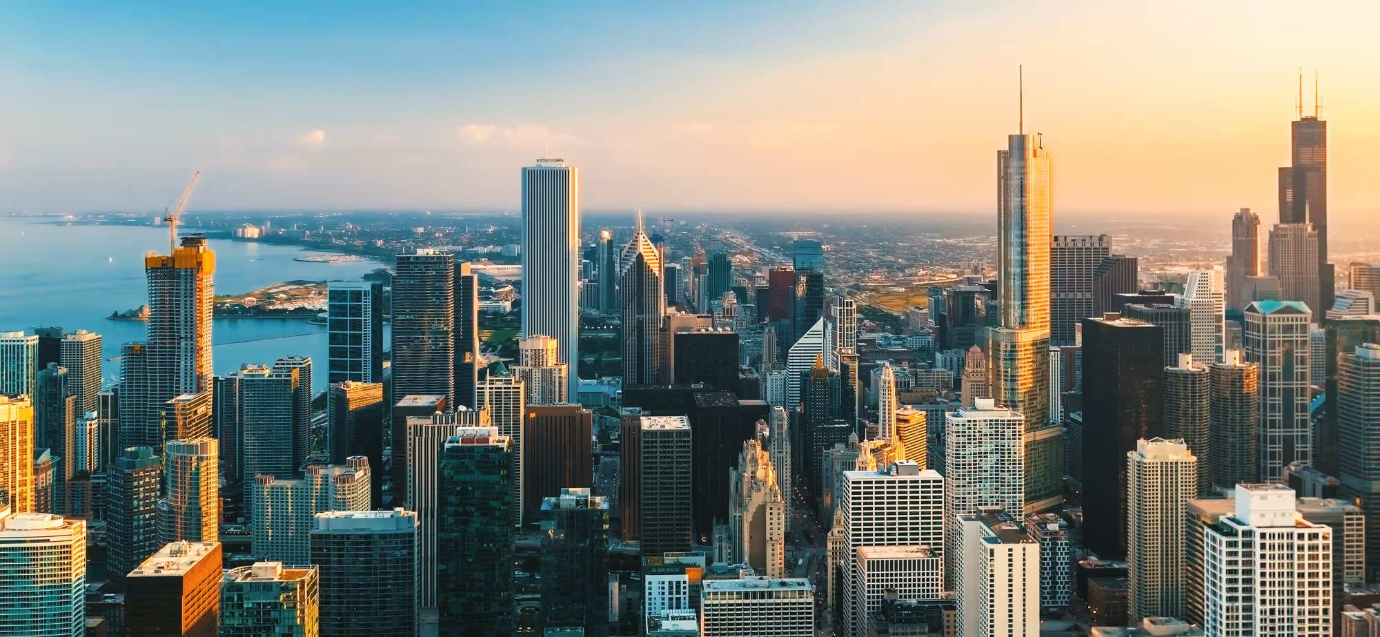 Aerial view of Chicago skyline at sunset with tall buildings and Lake Michigan in the background.