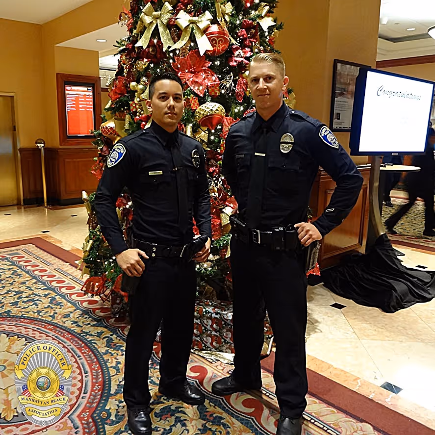 Two police officers in black uniforms standing in front of a decorated Christmas tree indoors.