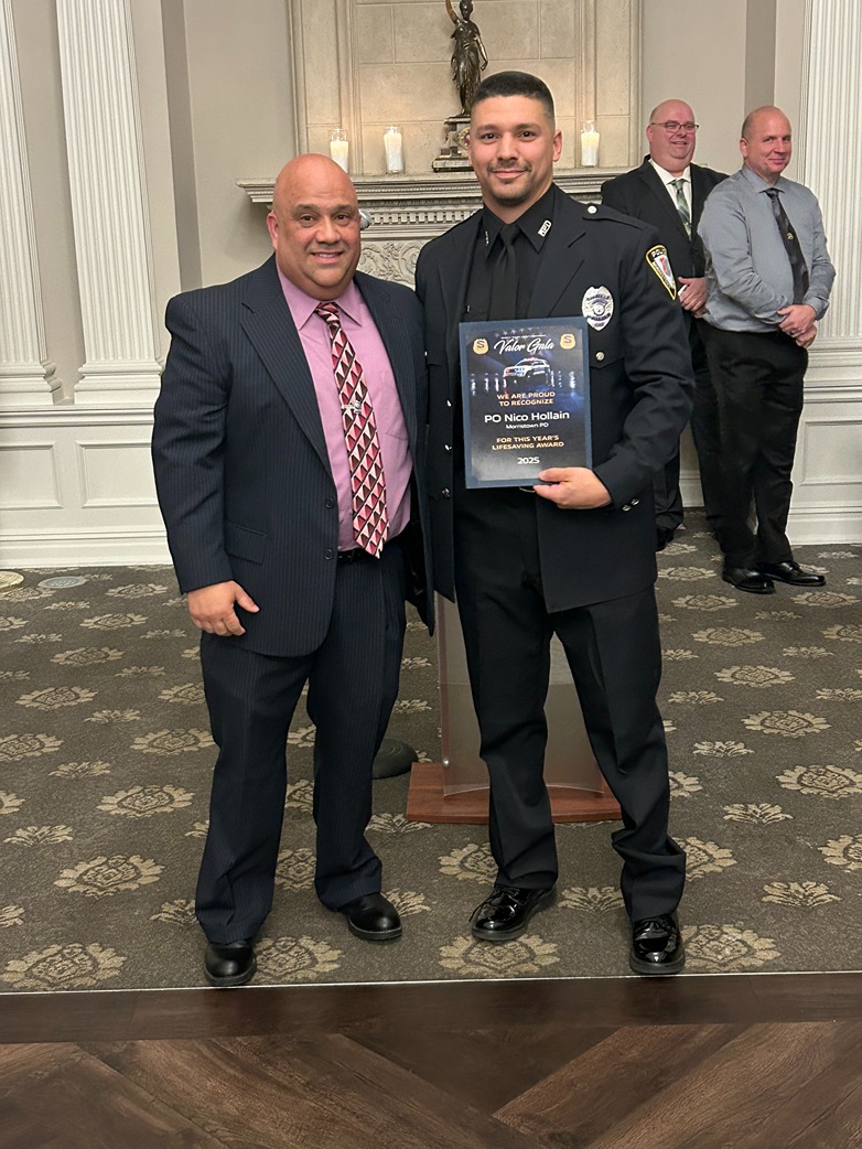 A man in a suit and a police officer holding a Valor Gala award plaque in a formal room.